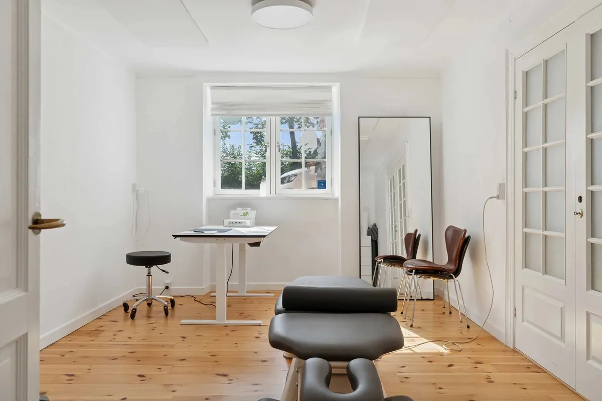 Kontor med højt loft, lysegul gulv og lysegrå vægge med en stor spejl og en skrivebord i et stille og soligt rum