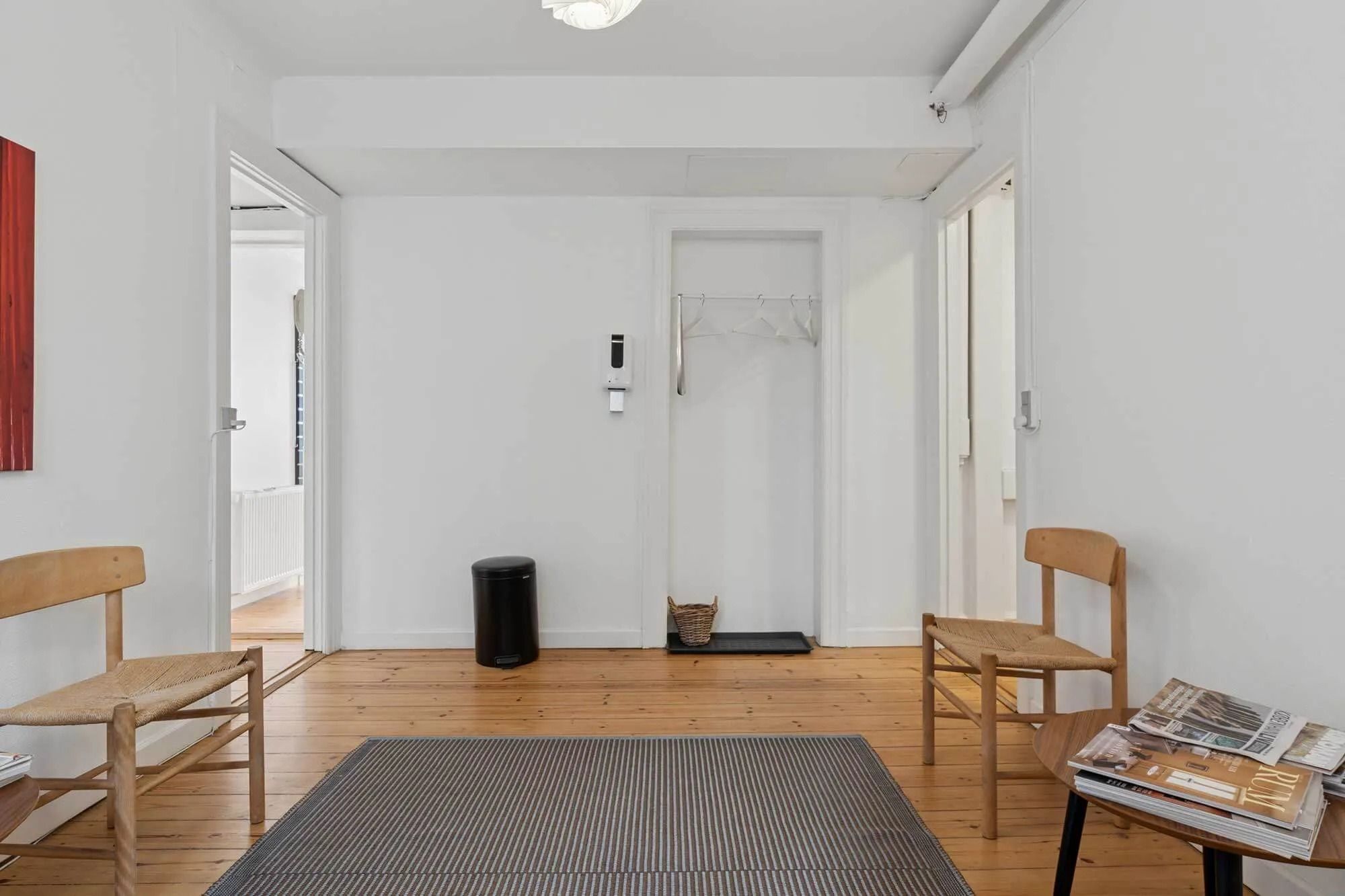 Indkørslet til et kontorlokal med to stole og en høj hylde med tidsskrifter og magasiner samt en papirkurv og en