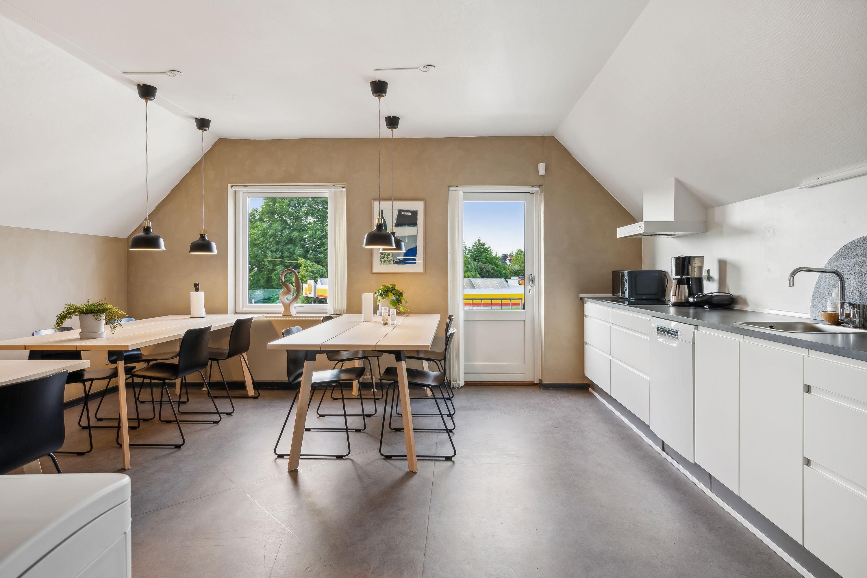 Lyst køkken med lyse lofter og vindue med udsigt til park, moderne hvide køkkenskabe og lyse træbord med stole