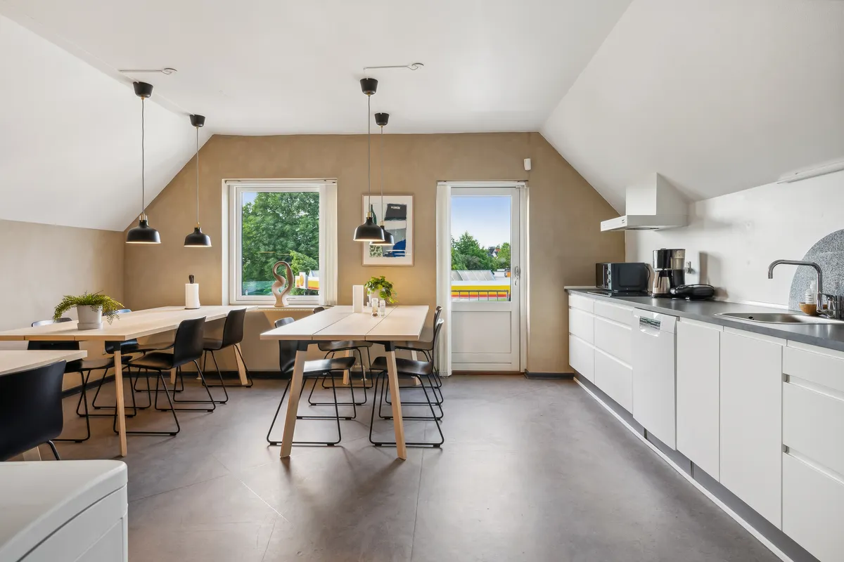 Lyst køkken med lyse lofter og vindue med udsigt til park, moderne hvide køkkenskabe og lyse træbord med stole