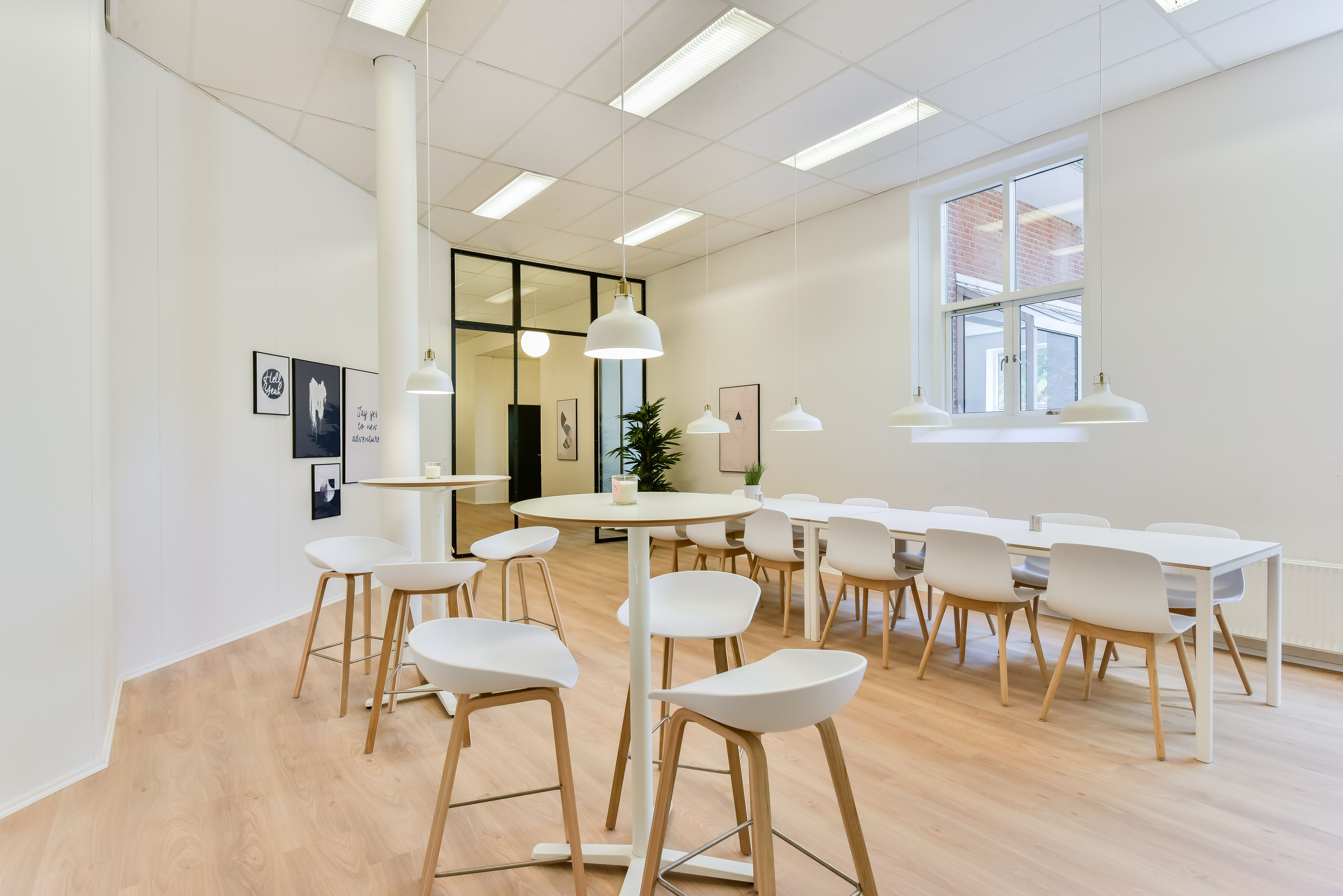 Kontorområde med lyse loftslampe, høje gulvvinduer og en stor bordgruppe for møder. De hvide stole og borde er lette at