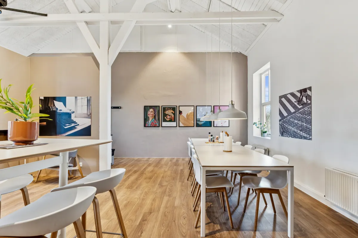 Kontorfællesskab med højloftet, hvid væg, plante, lysekroner, spisebord, stole, malerier, radiator, vinduesvisning og trægulv