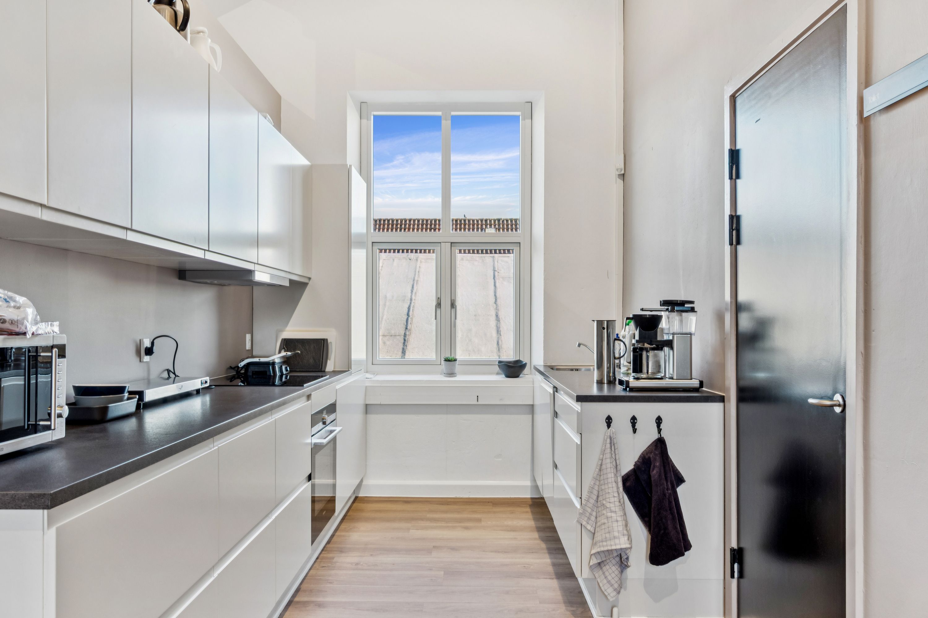 Moderne minimalistisk køkken med hvide vægge og trægulv, køkkenapparater og en spisestue med en stor vinduesdør