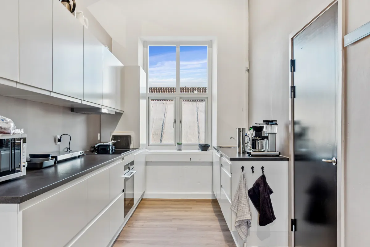 Moderne minimalistisk køkken med hvide vægge og trægulv, køkkenapparater og en spisestue med en stor vinduesdør