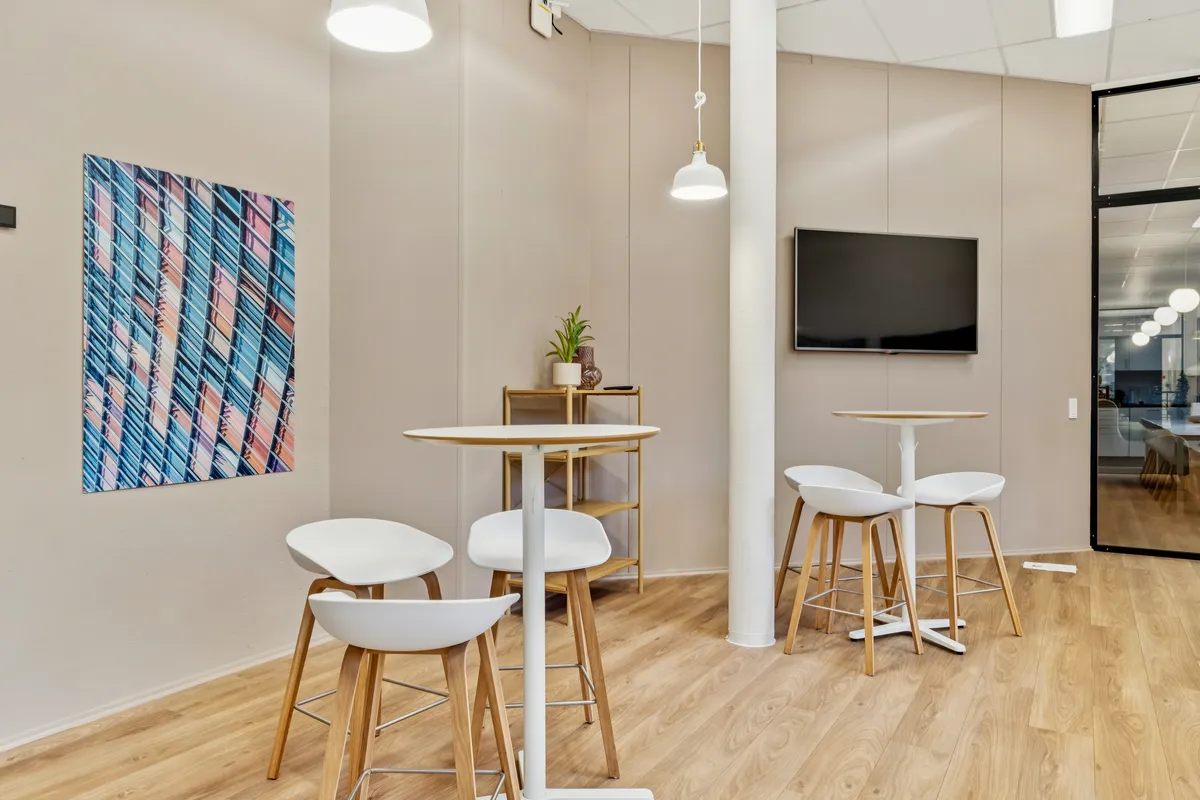 Kontorfællesskab med lyse, hyggelige møbler og en tv på væggen samt en dekorativ maleri med farverige linjer og farver