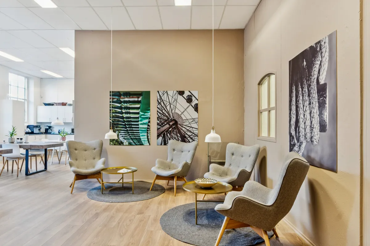 Kontorfællesskab med lyse lysekroner og smukke vægmalerier, flere læsestolhe og et bord med en skål på midten af gulvet