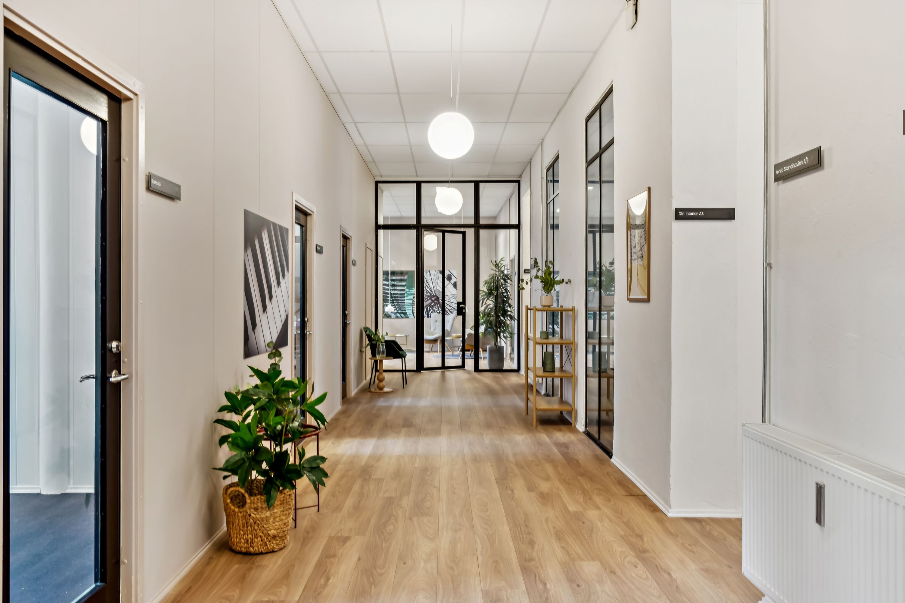 En lang og lys hall med åbne døre og glasruder, møbler og plantepotter, og lyse gulve og vægge