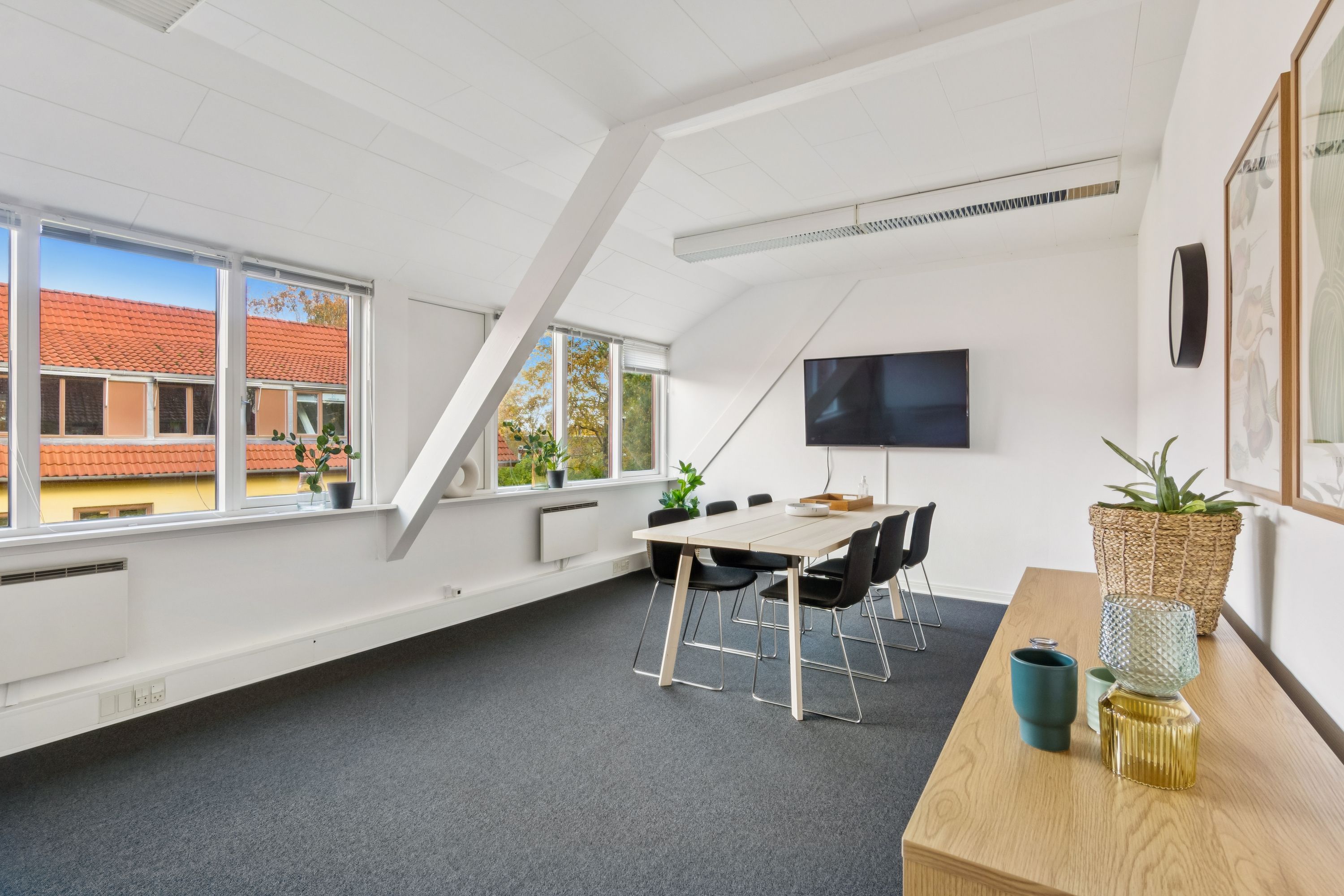 Kontorrum med vindue, hvidt loft, møbler, tv, indvendige planter og smukke udsigt til bygning med rød tagdækning