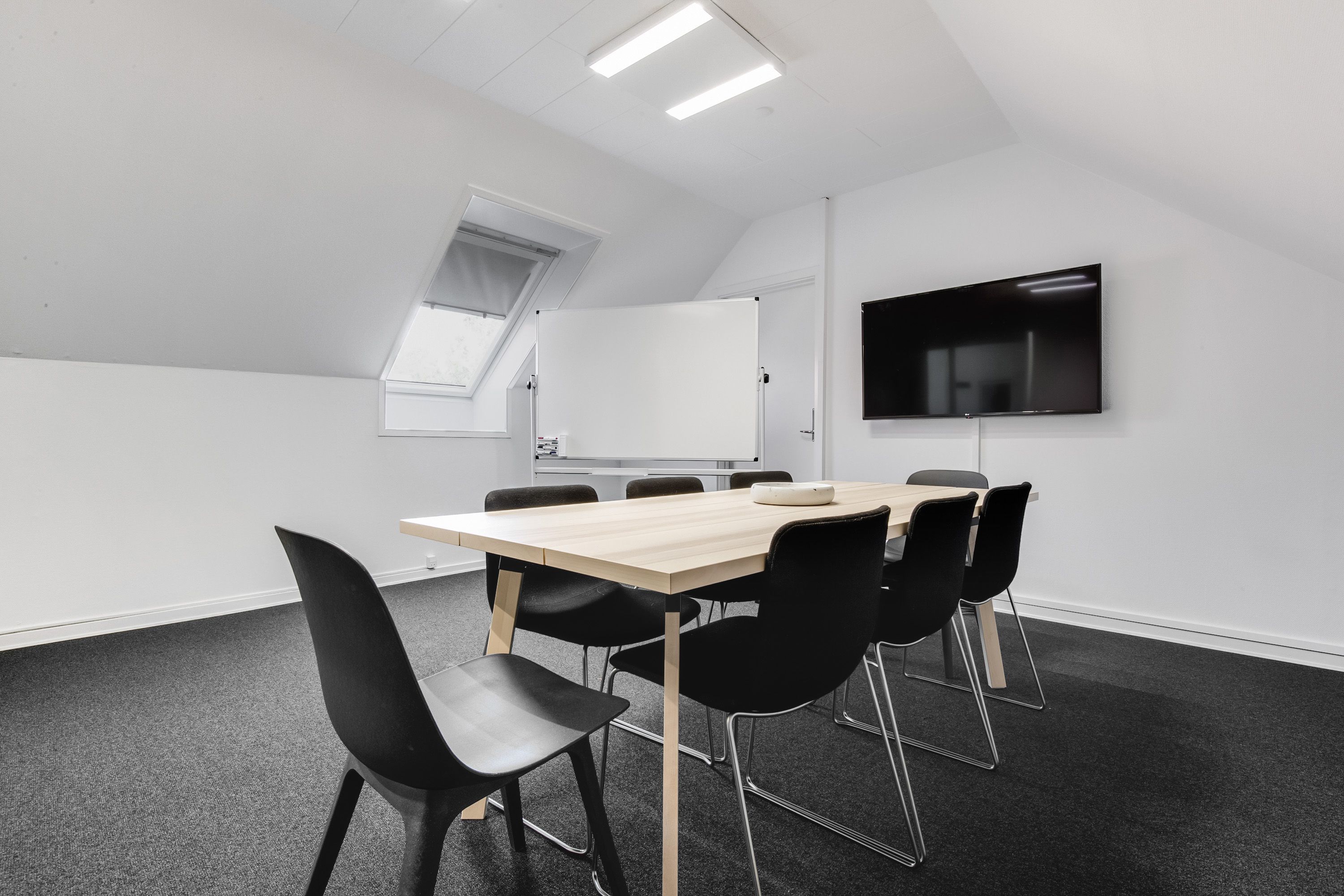 Møderum med højt til loftet og indbygget tv, to vinduer og lyse loftslamper