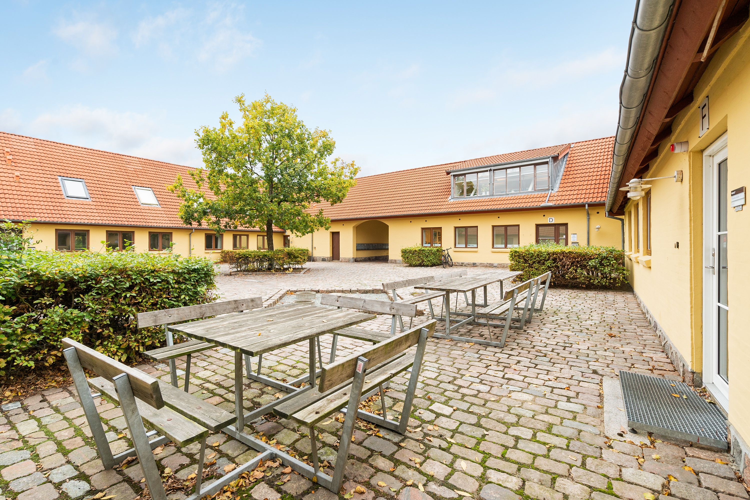 En parkeringsplads med fire bord og bænke, der er placeret under et hus med en rødt tag