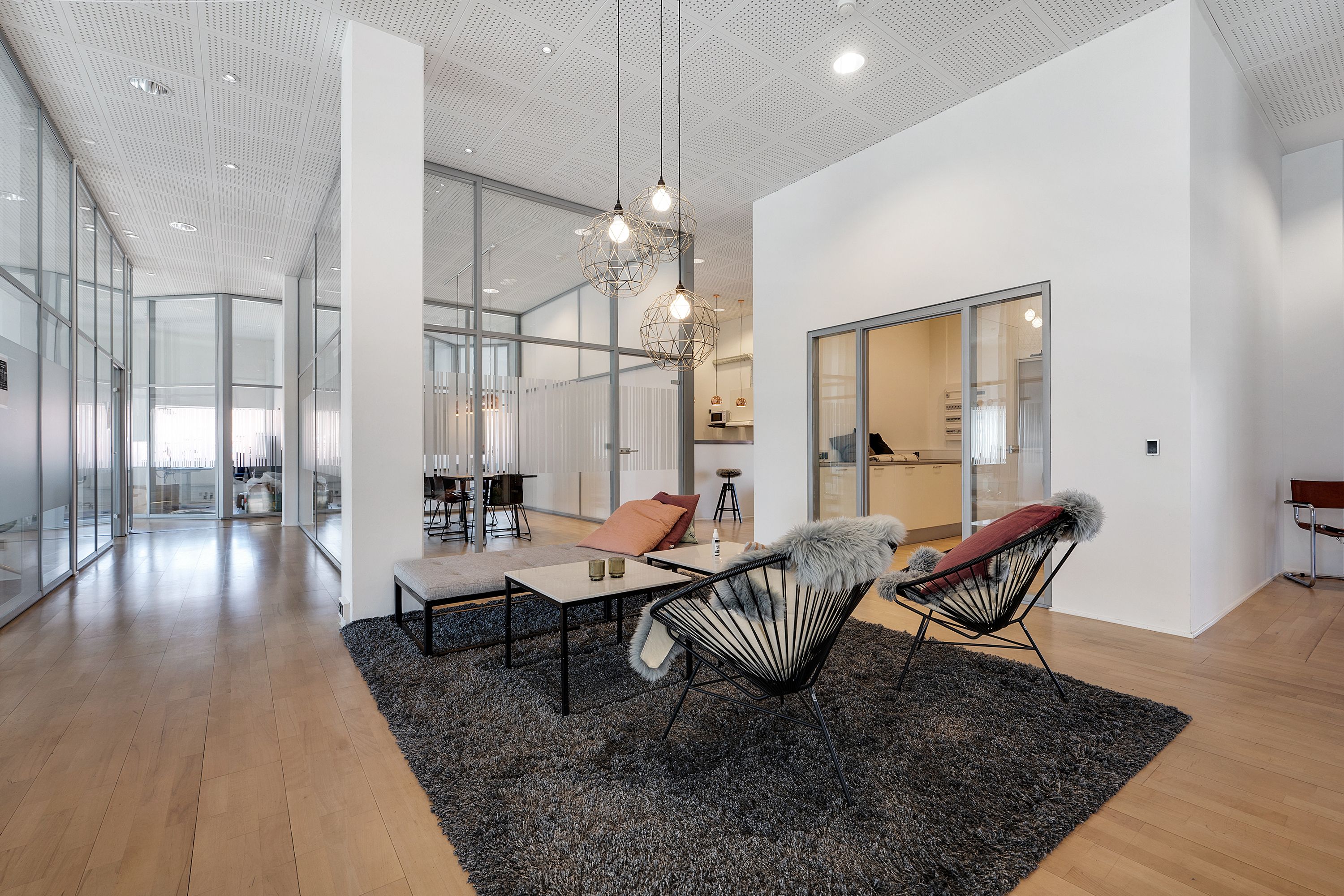 Moderne kontor med hvide vægge og lyse loftsprofiler, to stole med pelspuder og to kaffeborde, samt lysekroner i loftet