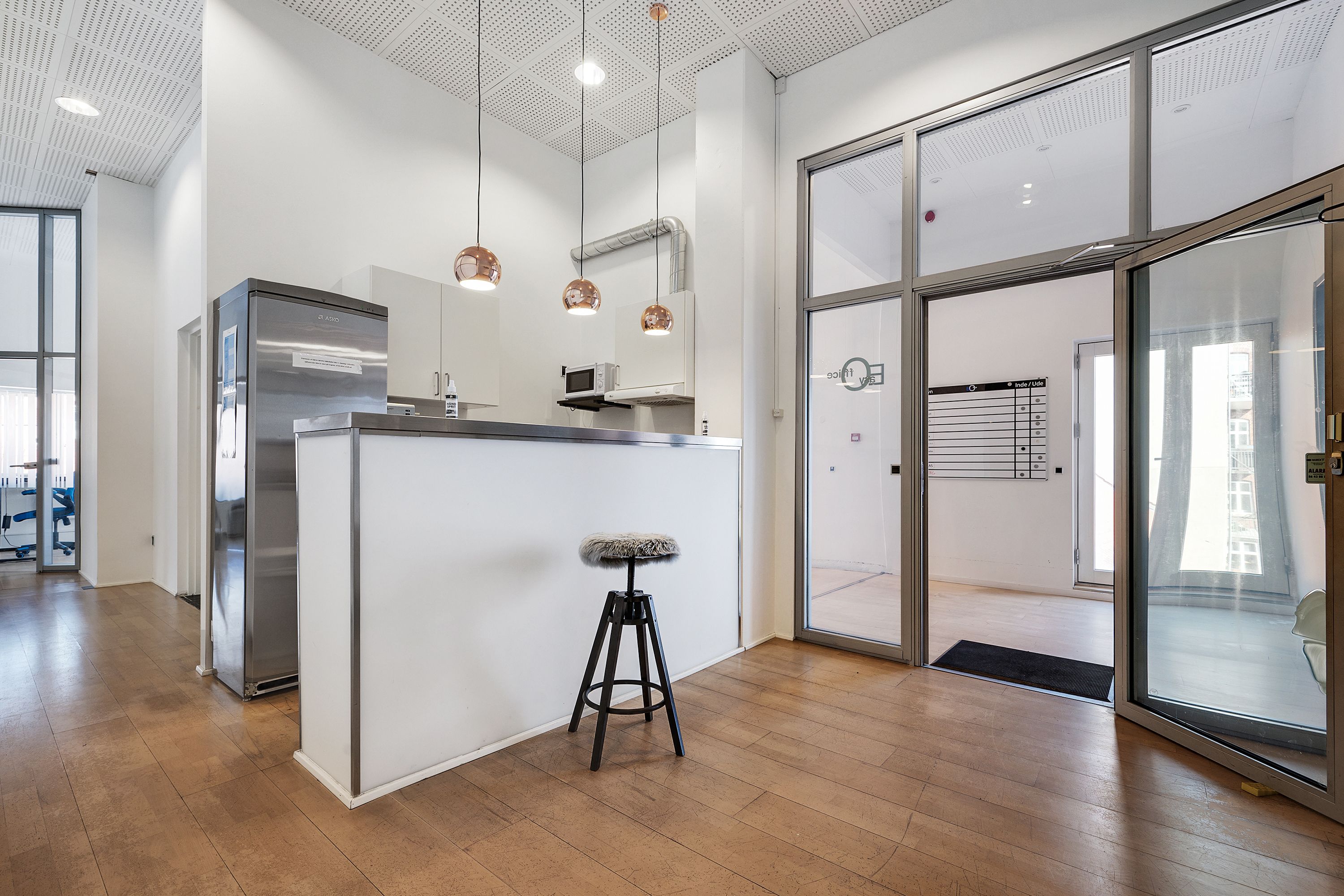 Moderne kontorlokaler med højloft og glasdøre og et stol med pelspude samt en køleskab og en mikroovn