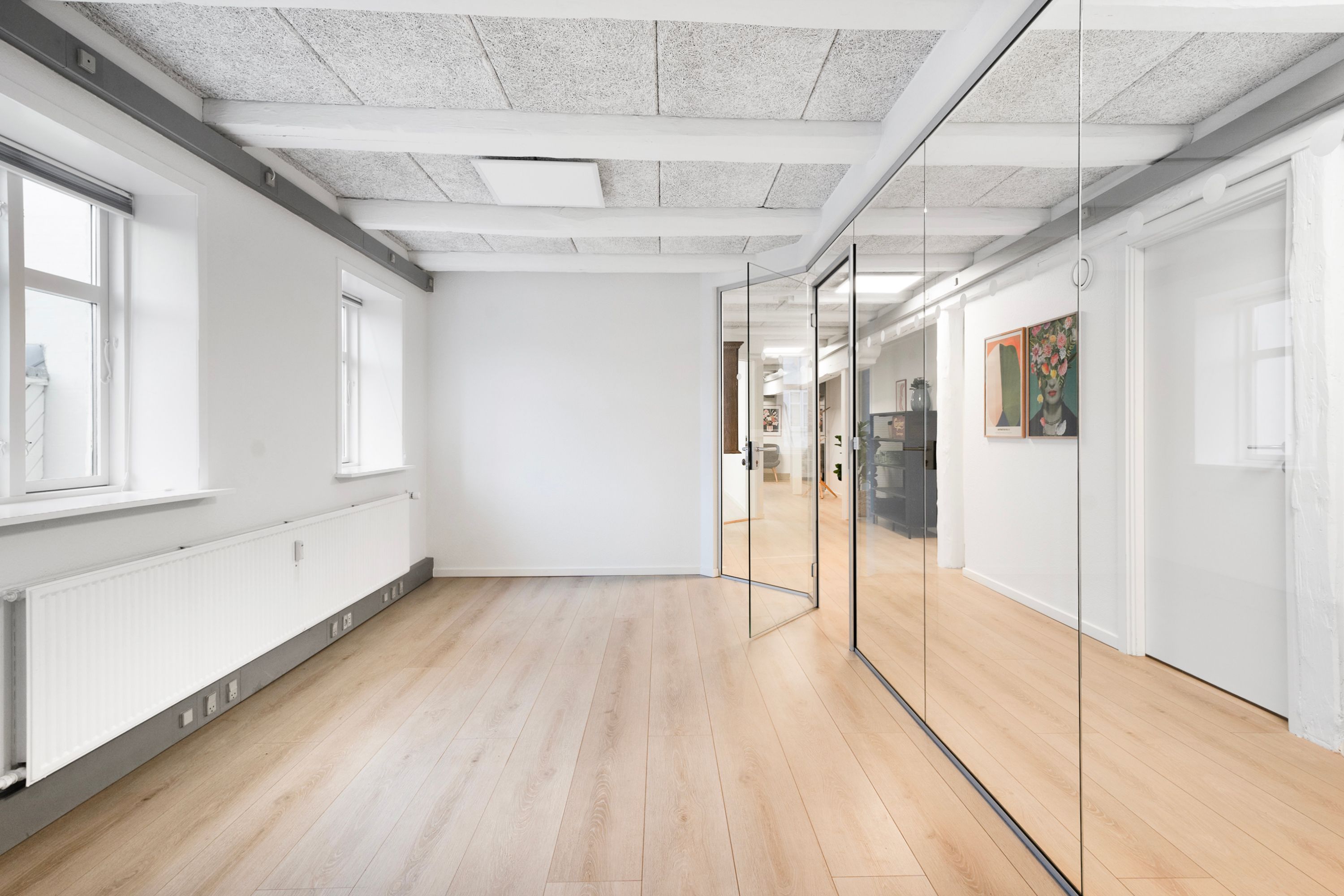 En stor rummelig kontorlokal med store vinduer, lyse lofter og trægulv samt to store spejlvægge og to malerier