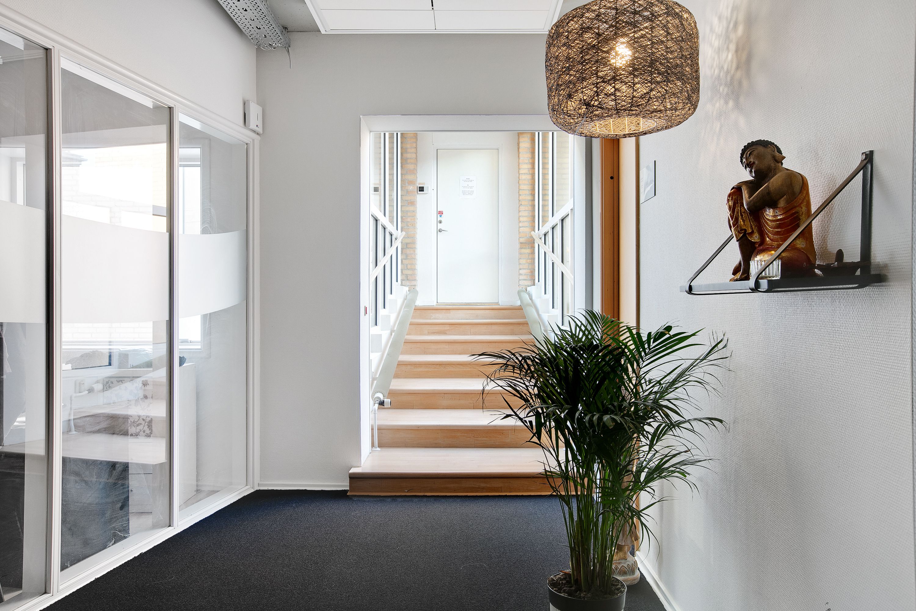 Kontorforretninger med glasdøre, moderne møbler, grønne planter og lyse gulve samt Buddha-statue og lysekroner