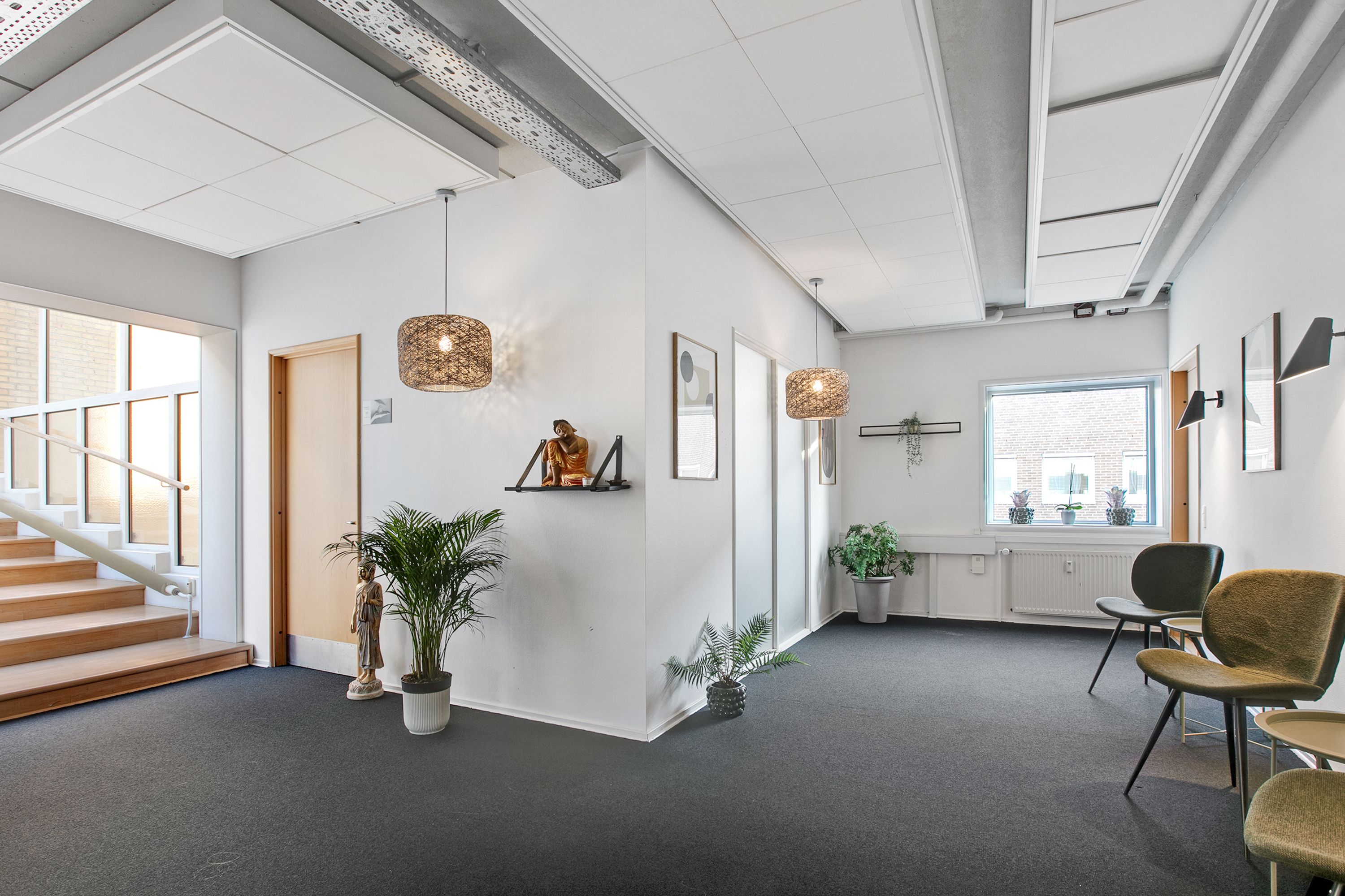 Inde i et lyst kontor med hvide vægge og lyse lofter, hvor der er to store buddhafigurer og lysekroner samt små plantepoter