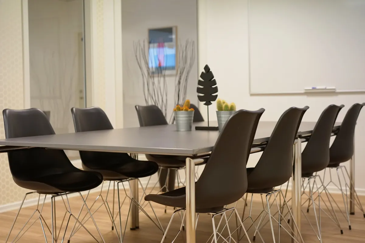 Kontor med gulv, møbler, plante og indretning, og en stor, tom væg med tavle og skriftstykke