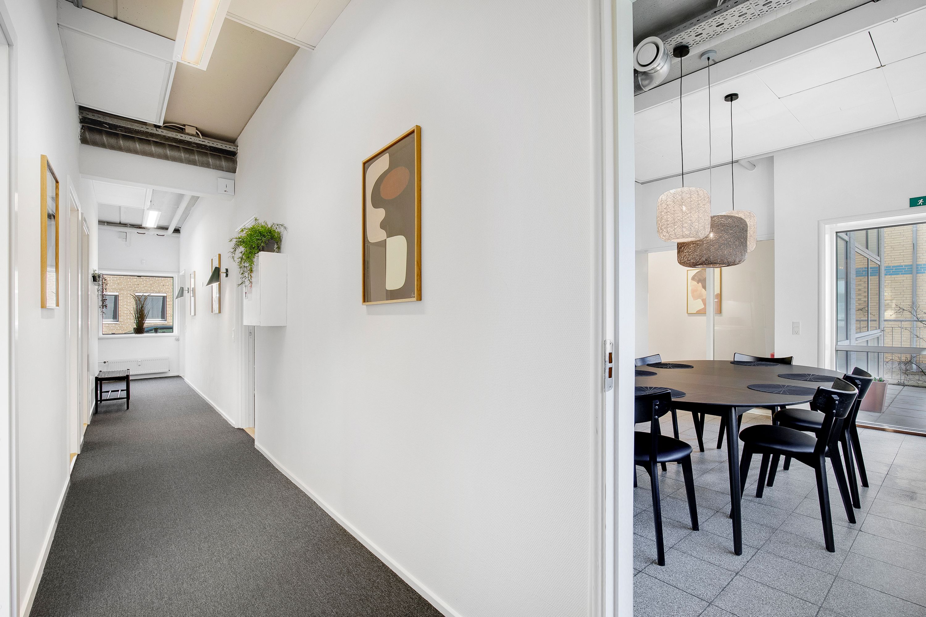 En mødelokale med runde bord og stole samt en kunstværk på væggen og plante i hjørnet