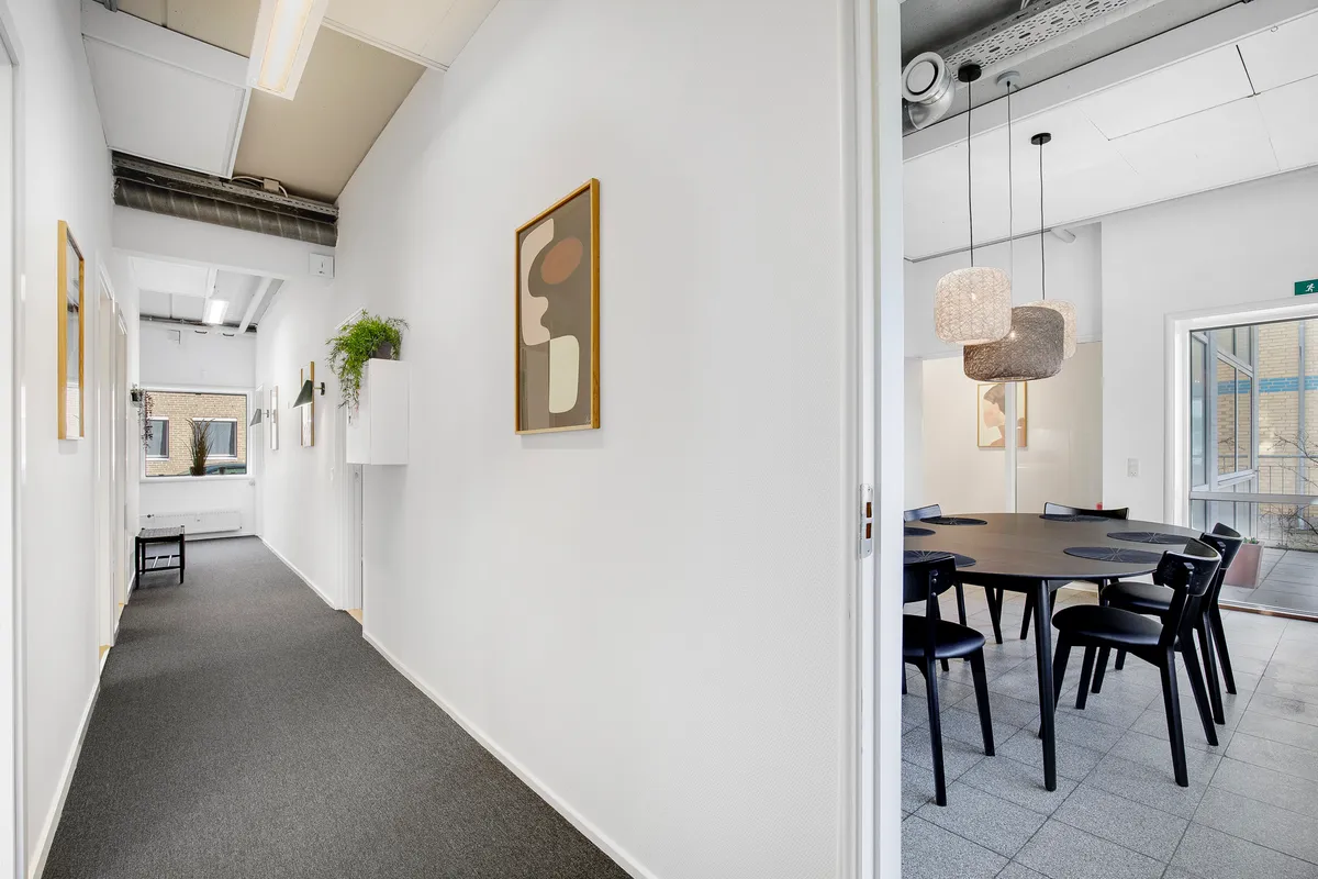 En mødelokale med runde bord og stole samt en kunstværk på væggen og plante i hjørnet