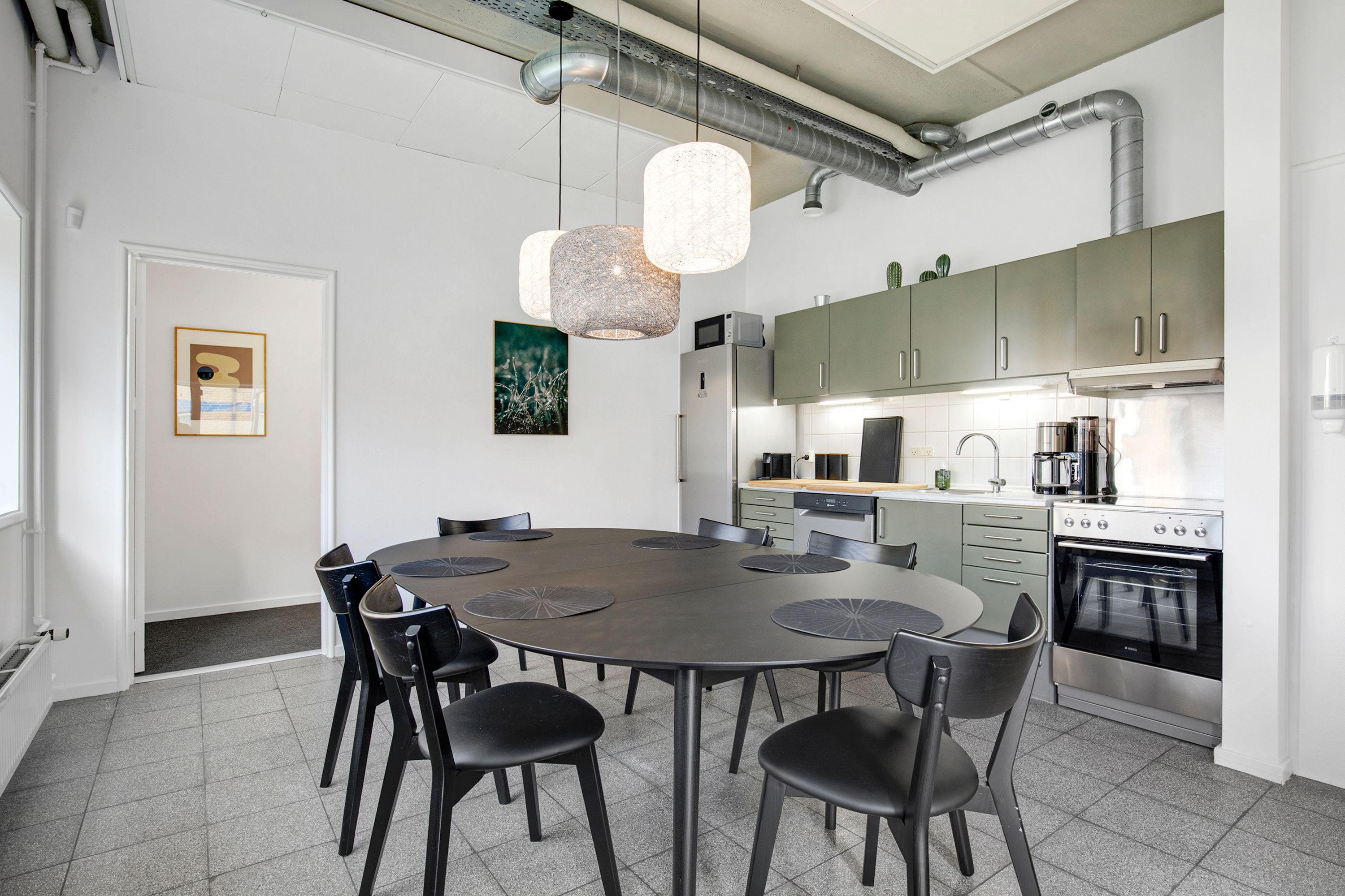 Kontorfællesskab med køkken og spiseplads med runde bord og stole, hængelampe og vægdekorationer