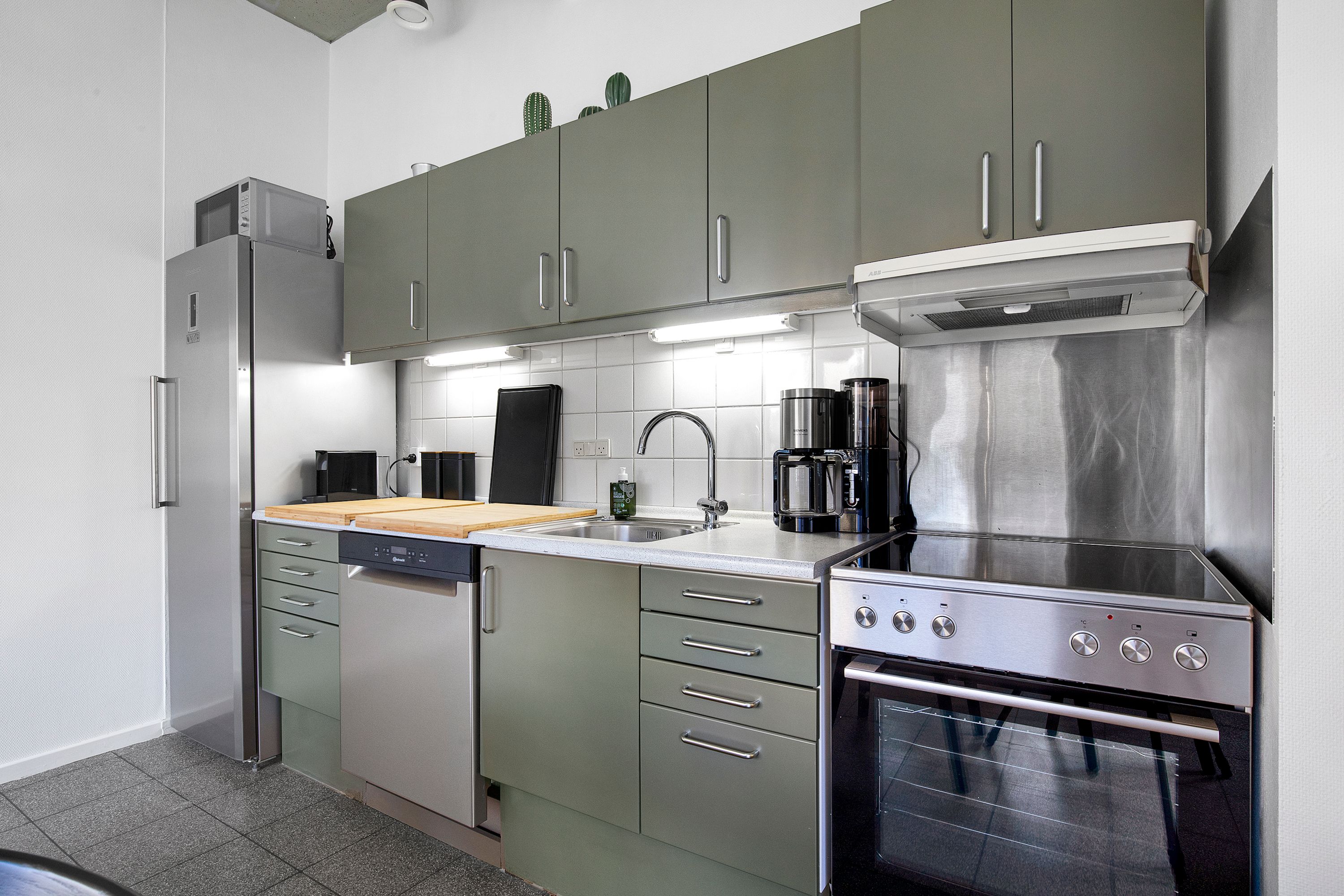 En moderne køkken med en køleskab, en ovn, en vaskemaskine, en kaffemaskine, en spiseplade og en hætte over kogepladerne