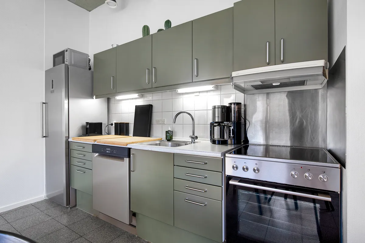 En moderne køkken med en køleskab, en ovn, en vaskemaskine, en kaffemaskine, en spiseplade og en hætte over kogepladerne