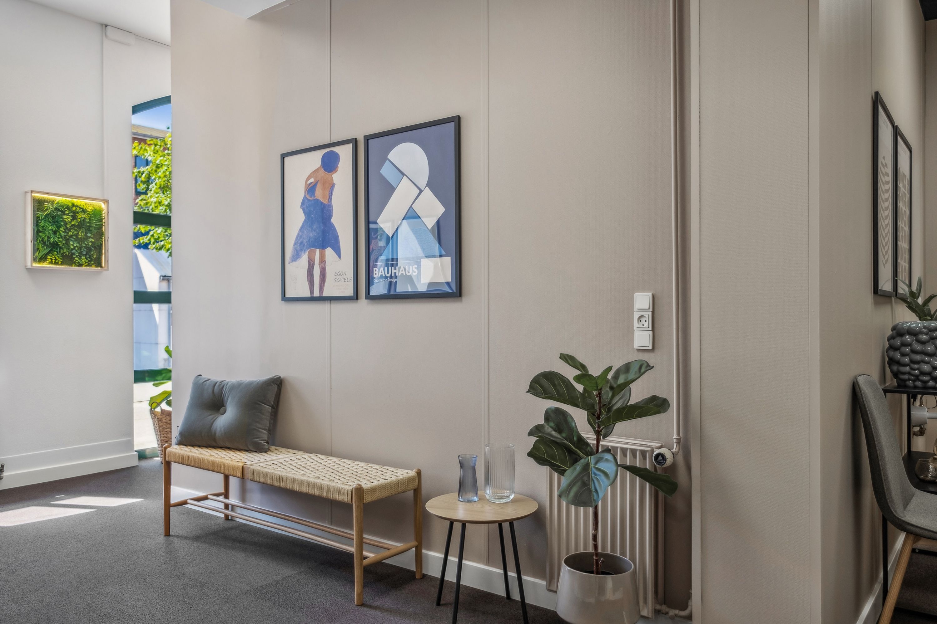 Et lyse og moderne indgangsområde med en komfortabel bænk og et lille sidebord med to glasser og en plante