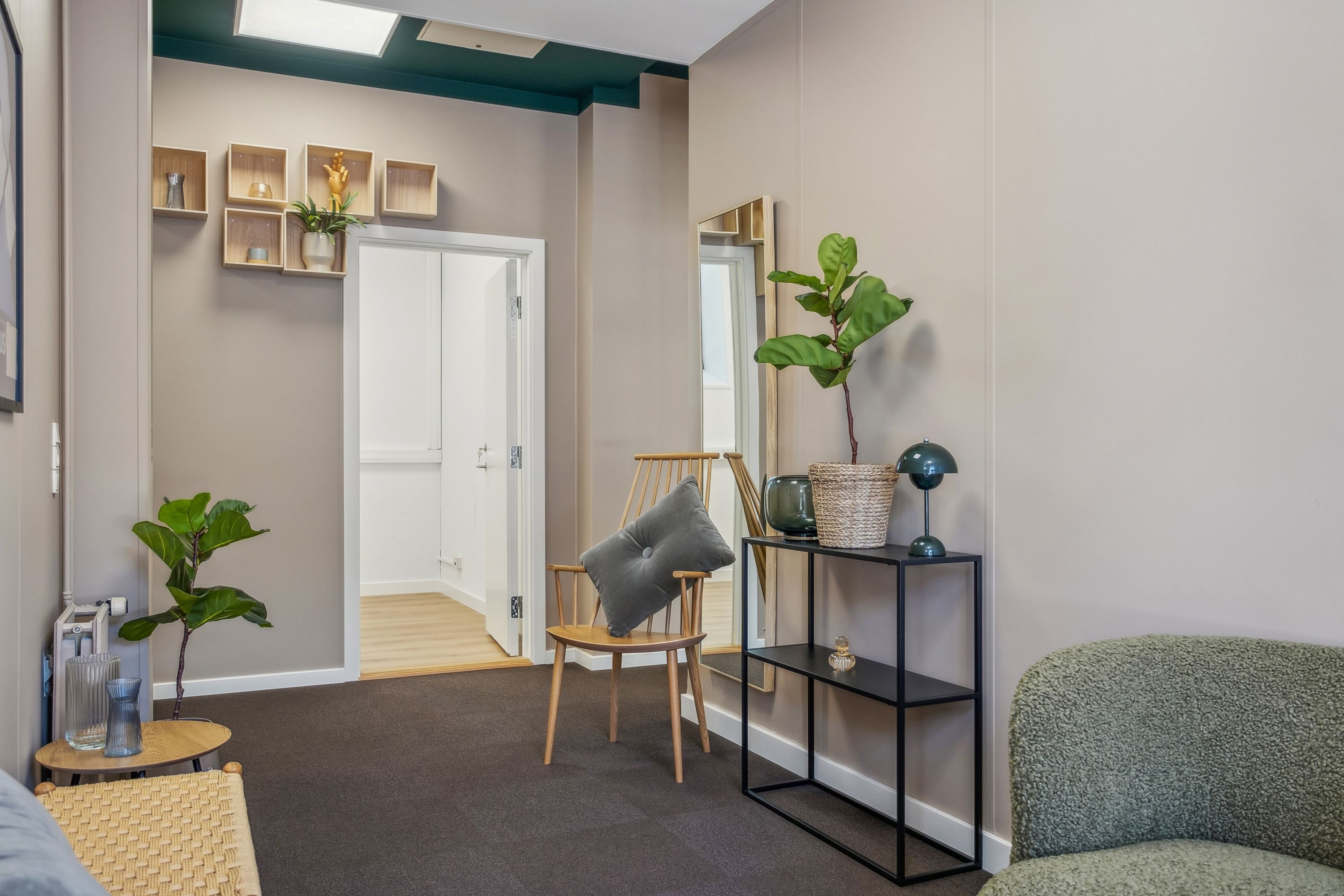 En moderne lobby med beige vægge, trægulv og plantehylderne. Der er et spejl og et bord med en plante og lamper.