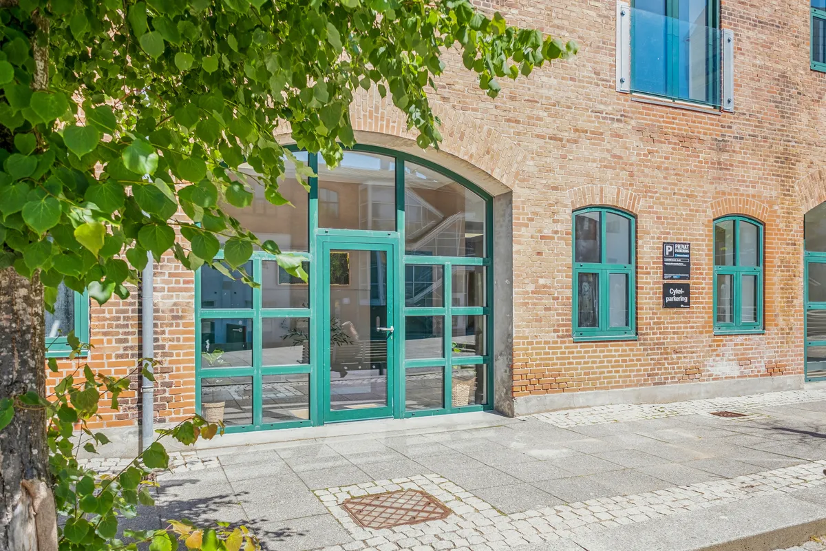 Bygning med glasruder og grønne vinduer, hvor den ene udgang er åben og indeholder en grøn dør med stang. Der er også et