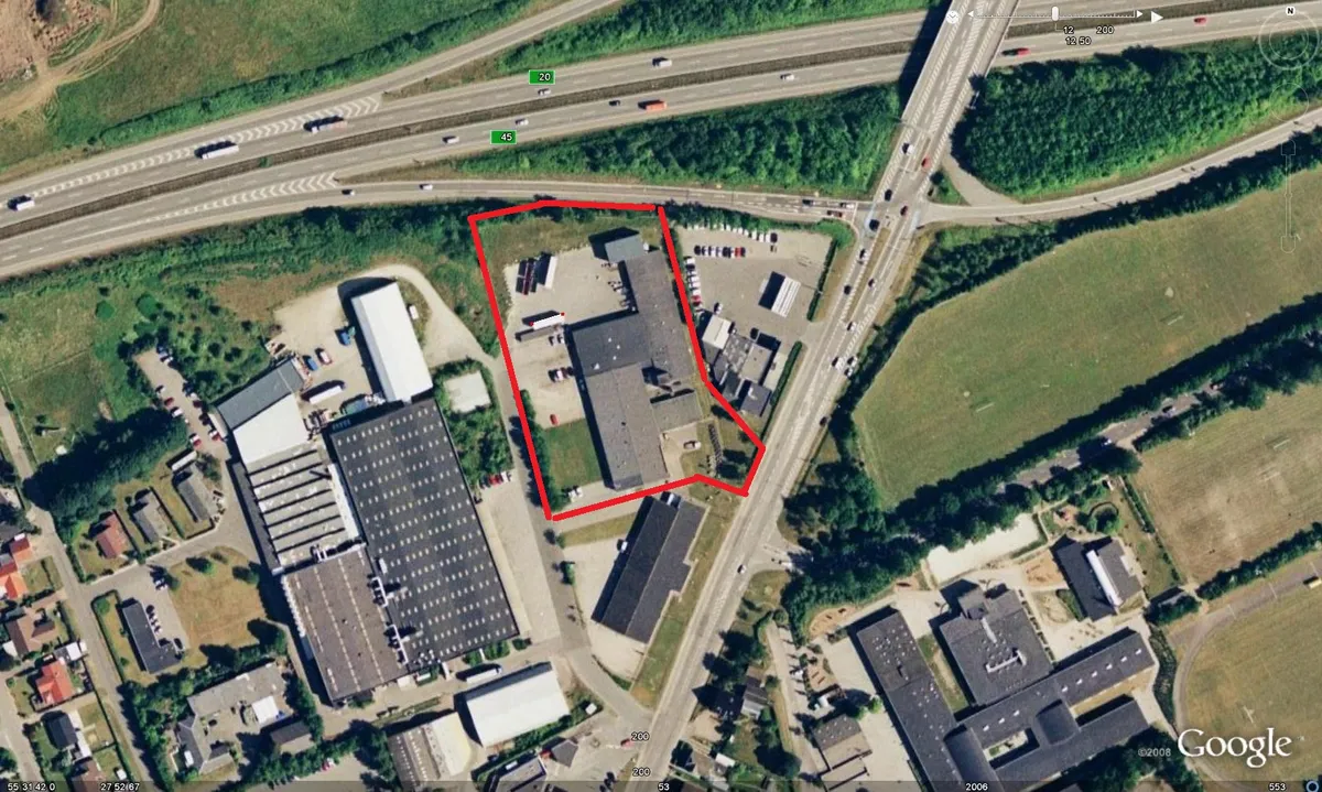 Område med bygninger og parkeringspladser nær motorvejen i Kolding, med en rødt markeret zone og et hus med garagedør