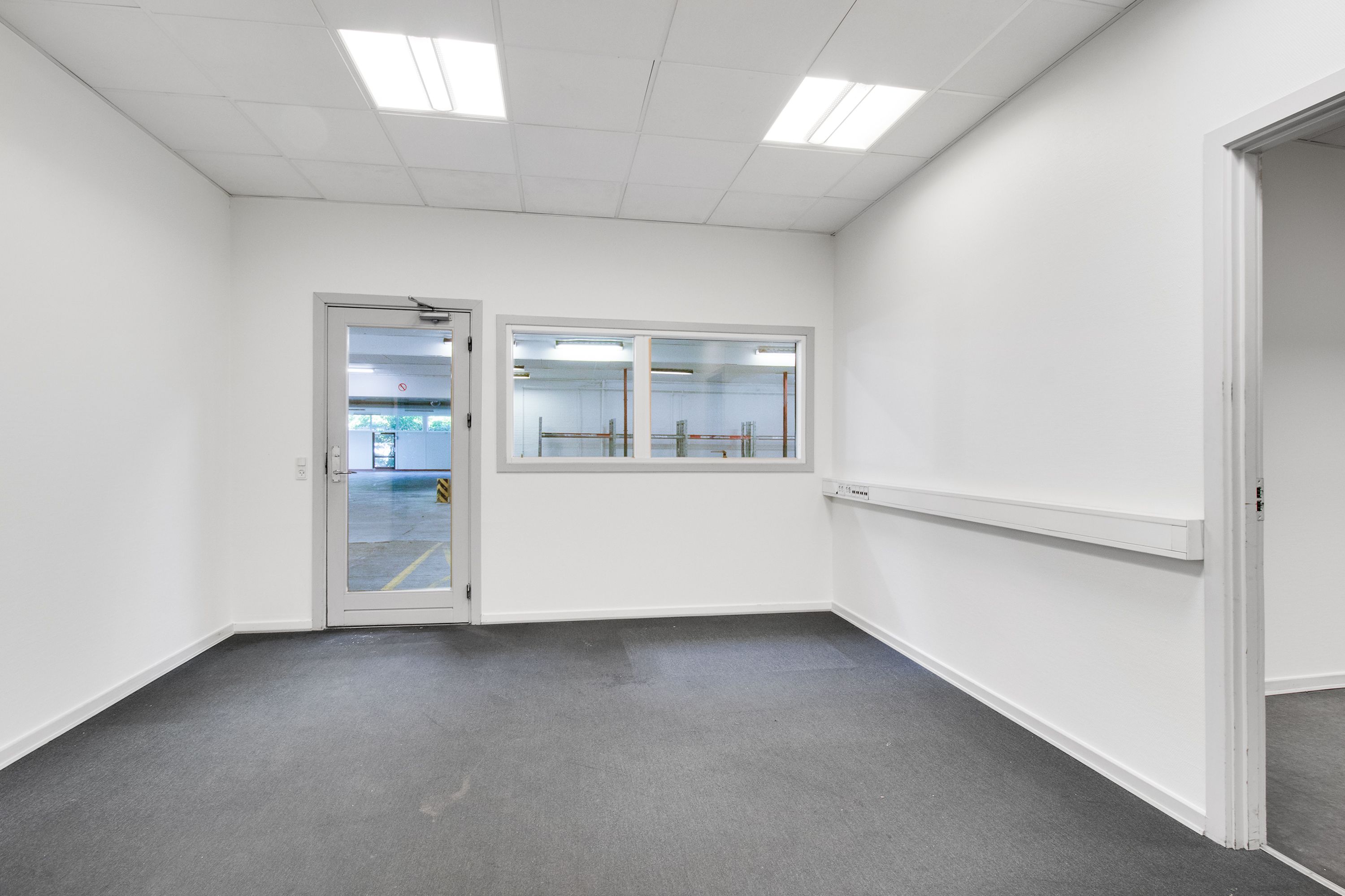 Lagerrum med hvide vægge og gulv, hvor vinduet og døren er åbne. Der er en stribet gulv og en hvid væg med elektriske