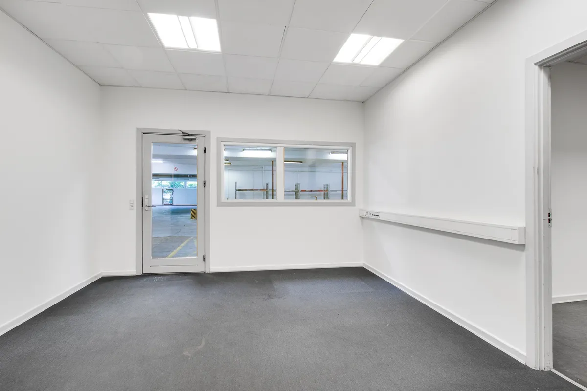 Lagerrum med hvide vægge og gulv, hvor vinduet og døren er åbne. Der er en stribet gulv og en hvid væg med elektriske