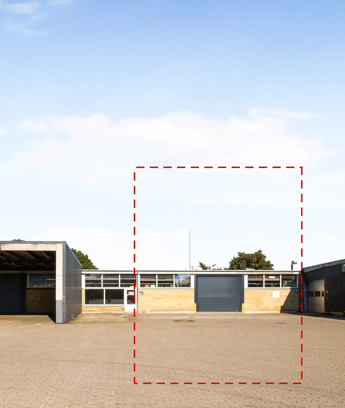 Lager med garagedør og vinduer på den ene side og en stor tom plads på den anden side