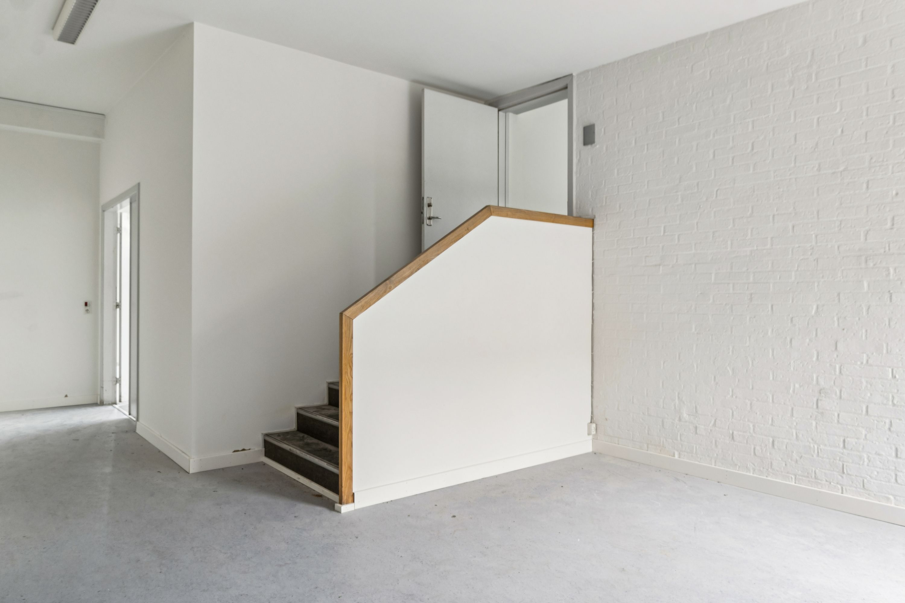 Et minimalistisk, hvidt interiør med træforstærket trappeforløb, blanke gulve og hvide vægge med teglstensmønster