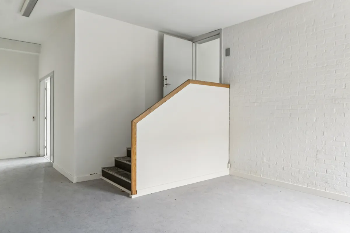 Et minimalistisk, hvidt interiør med træforstærket trappeforløb, blanke gulve og hvide vægge med teglstensmønster