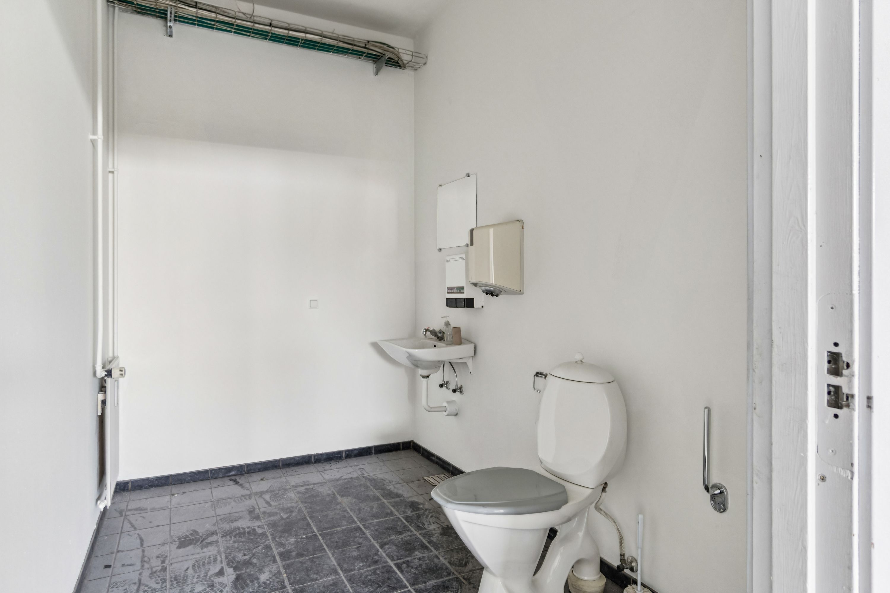 Et lille toilet med et hvidt toilet, en hvid vask og et håndklædeapparat på væggen, der er hvide og lavet af keramik