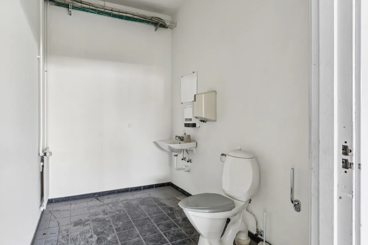 Et lille toilet med et hvidt toilet, en hvid vask og et håndklædeapparat på væggen, der er hvide og lavet af keramik