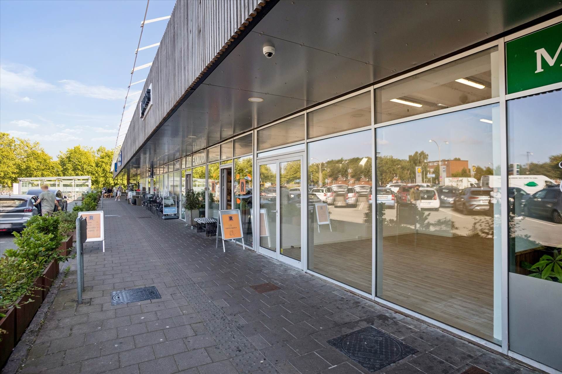 Lejemålet med udsigt til parkeringsplads og skov. Glasser og skilte langs gaden. En person går ind i et butikslokal med