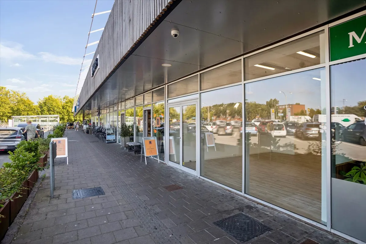 Lejemålet med udsigt til parkeringsplads og skov. Glasser og skilte langs gaden. En person går ind i et butikslokal med