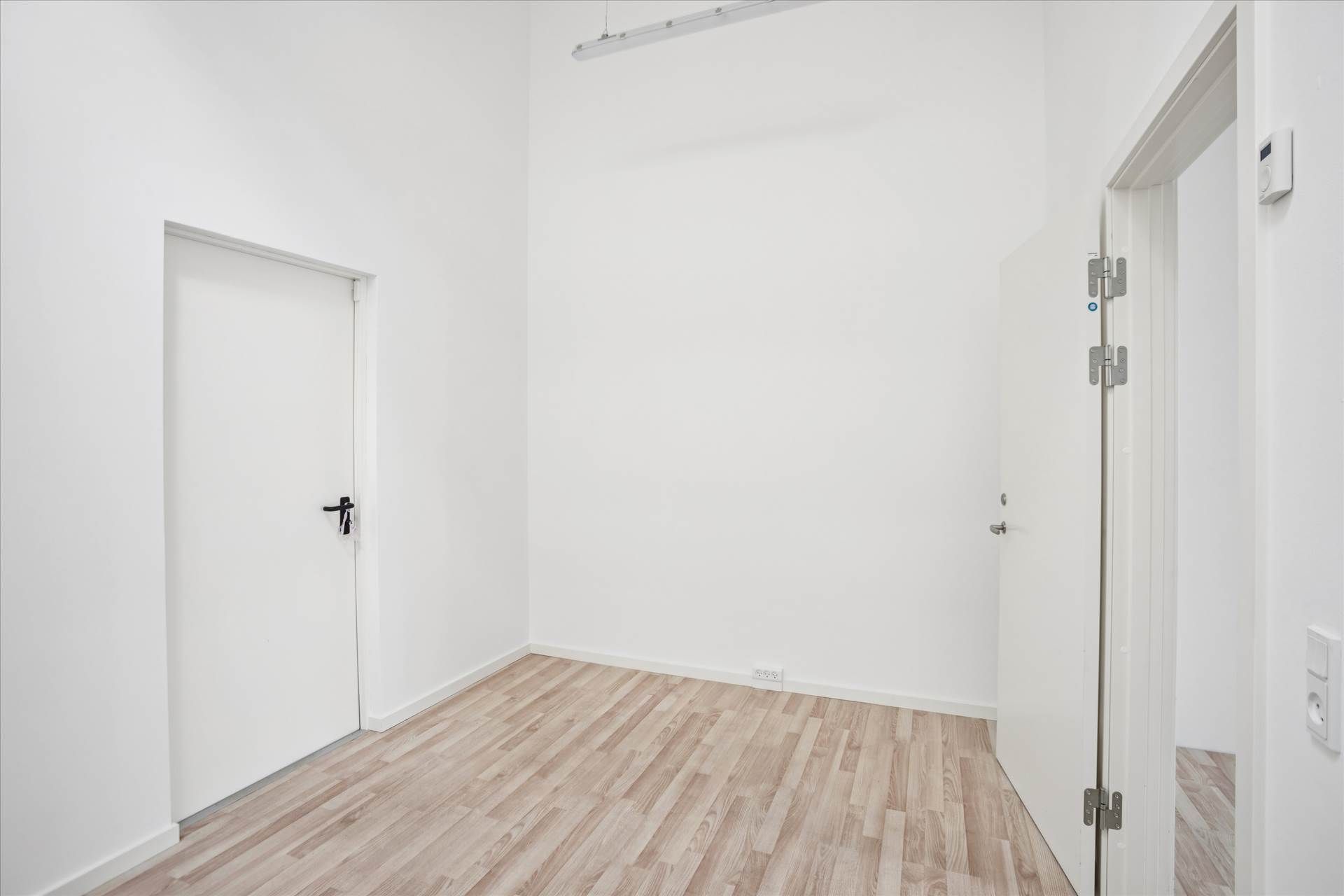 Ledig lokale i et moderne bygning med hvidt væg og gulv og to hvide døre med håndtag og hængsler