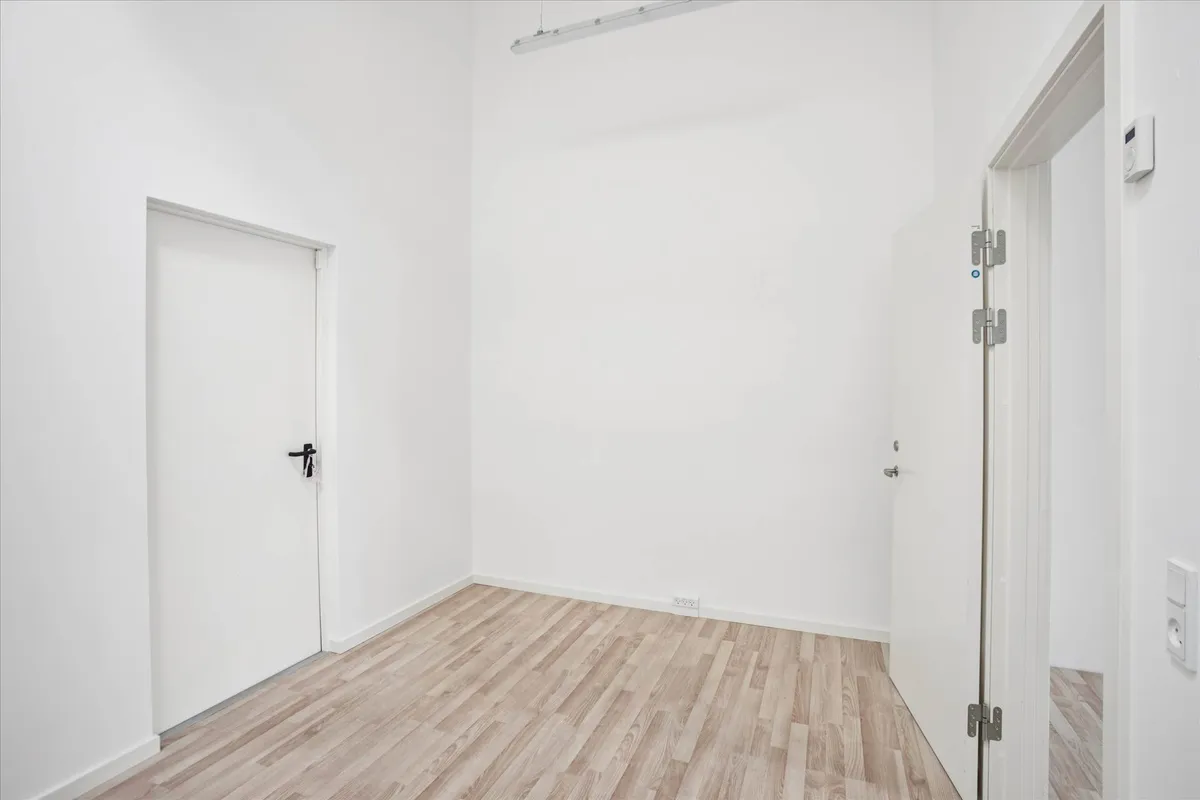 Ledig lokale i et moderne bygning med hvidt væg og gulv og to hvide døre med håndtag og hængsler