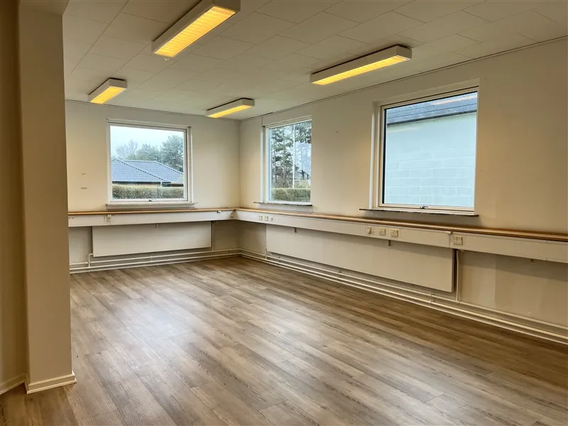 Erhvervslokaler med lyse gulve, hvide vægge, store vinduer og indbygget belysning. Lokaler med slanke, lysebrune