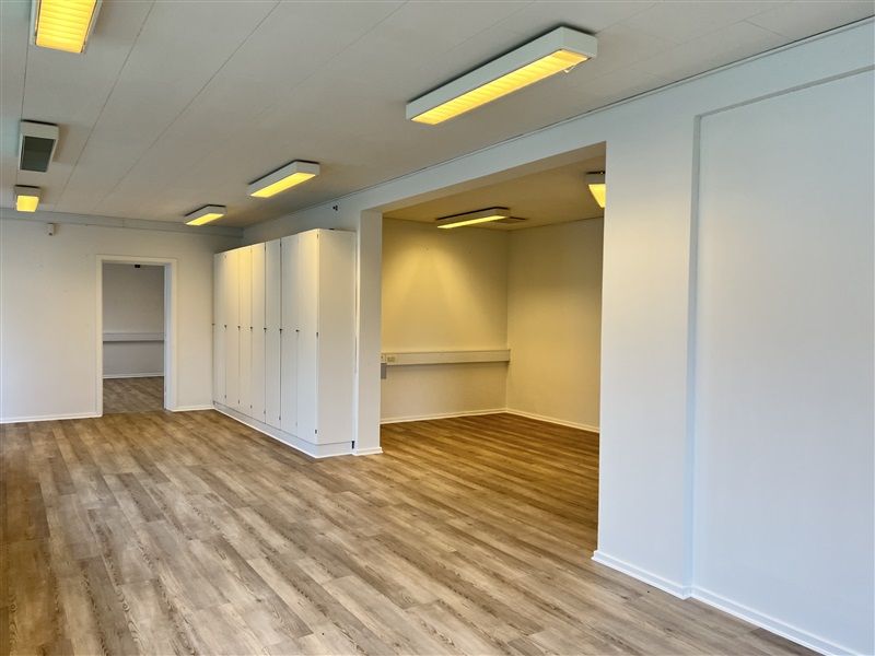 Foto af en moderne kontorlokation med højt hvide loft, hvilket skaber et lyst og åbent rum. Rummet er pænt oplyst med hvide