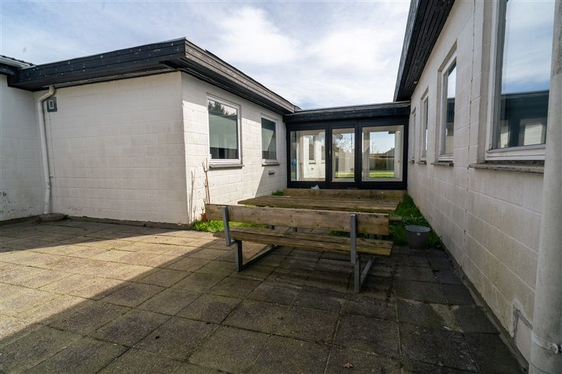 En moderne hvid bygning med en terrasse, der har et træbord og en bænk samt glasdøre