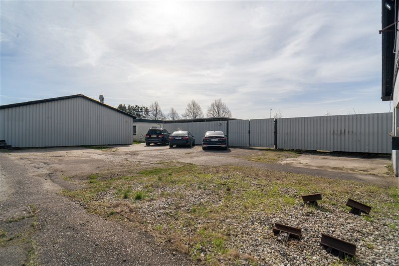 Kontorbyggeri med flere parkerede biler og en lukket port, med græs og grus på forsiden