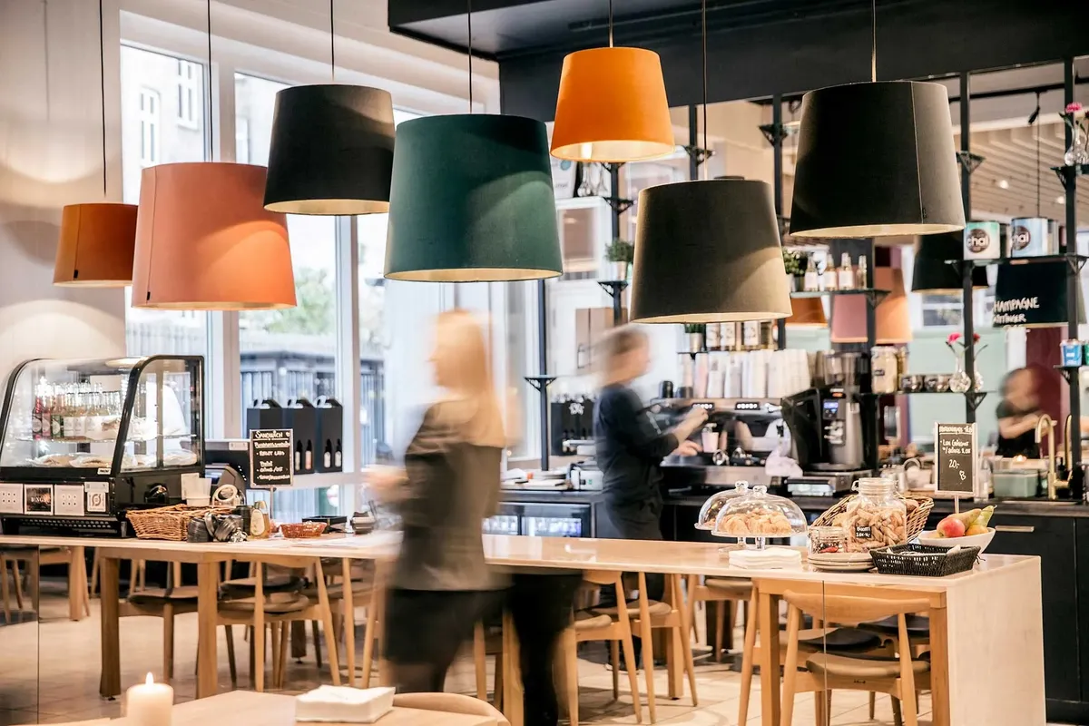 Lyse loftslamper i forskellige farver og en kvinde, der går i en café med røde frugter og småkager