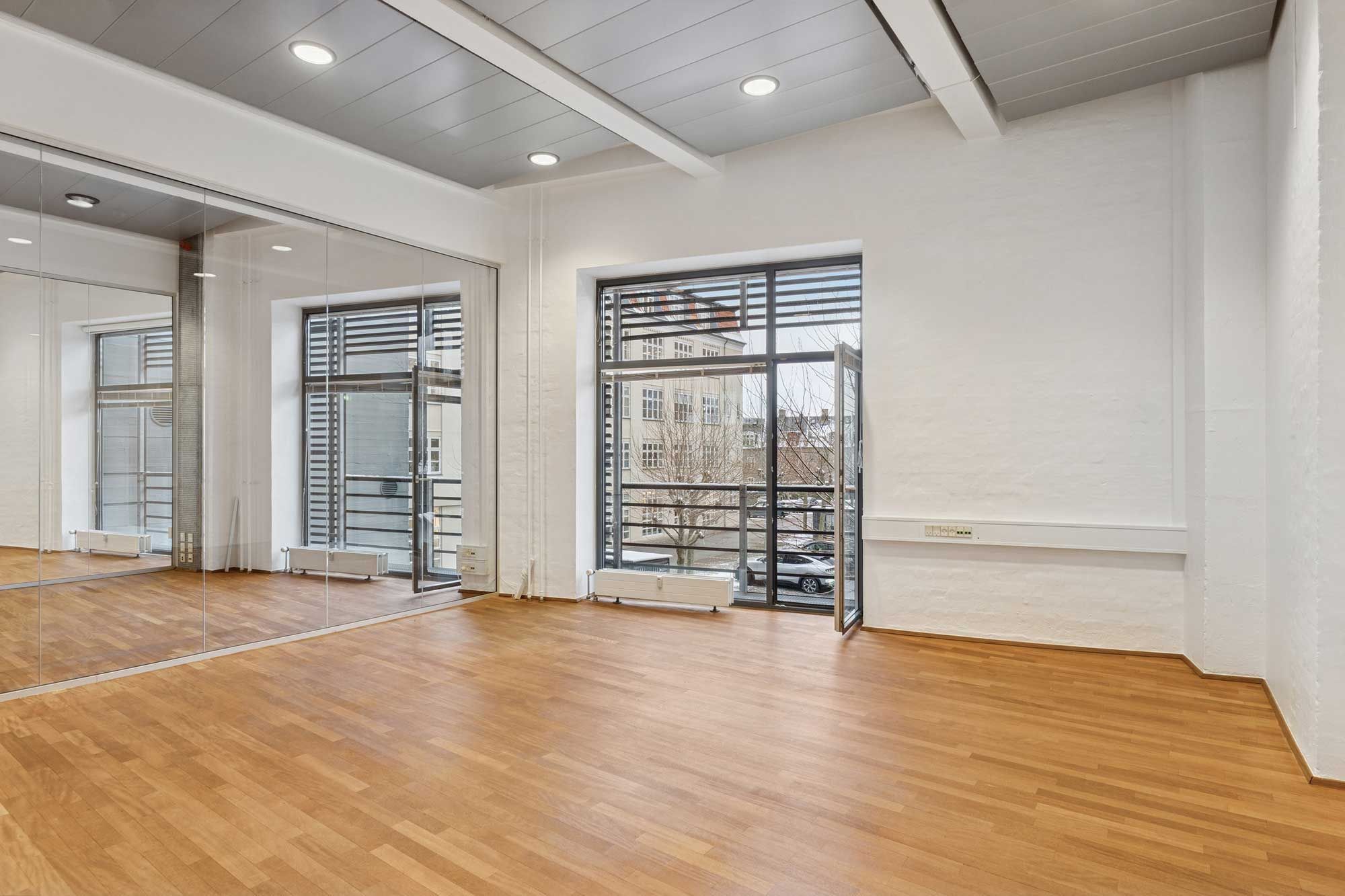 Store, lyse kontorrum med hårdt trægulv og glasvægge og døre samt højt hvælvet loft med indlejrede runde lyskatler