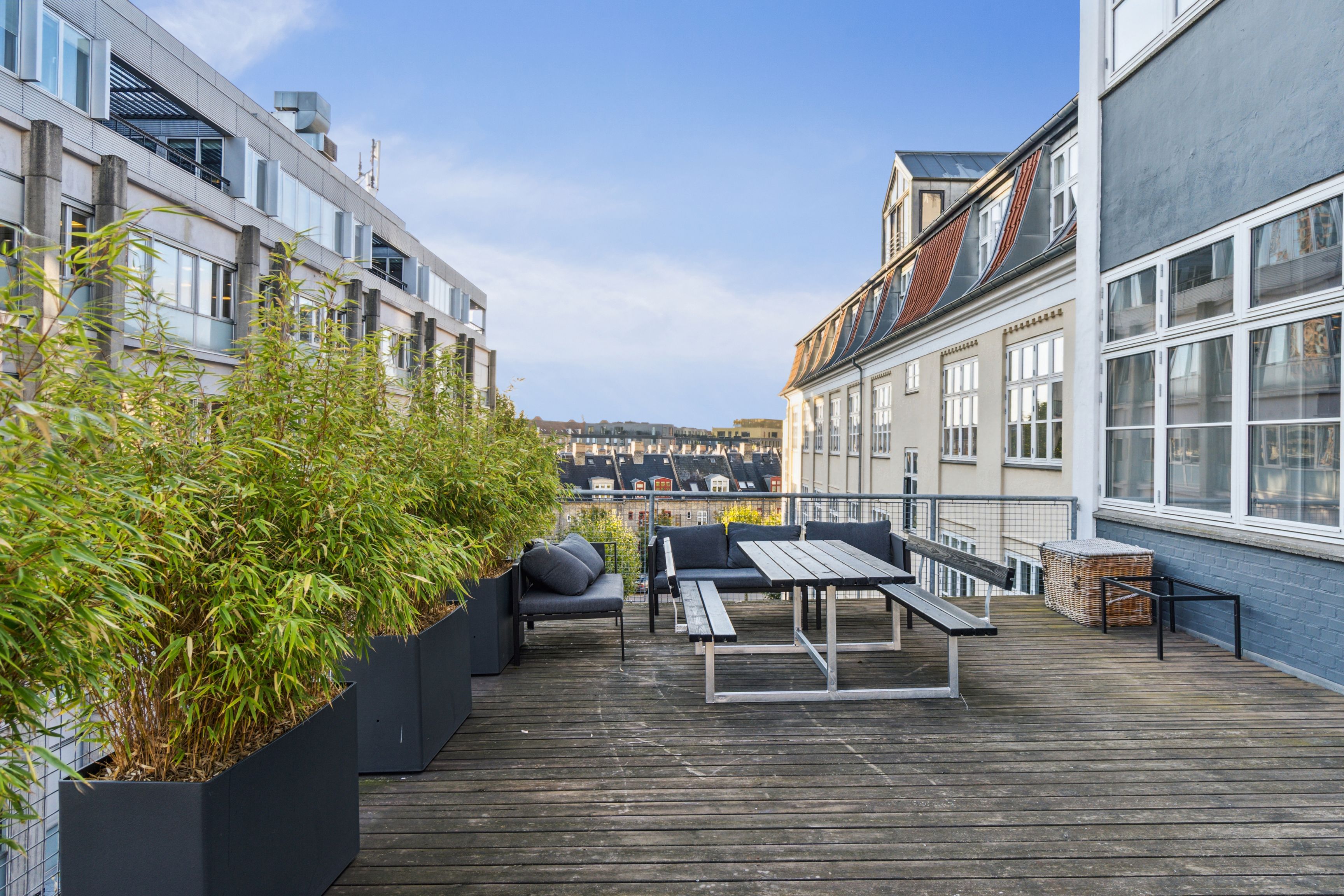 Terrasse med trægulv og møbler, hvor to stole og en bord er placeret, og to høje plantekasser er stillet op.