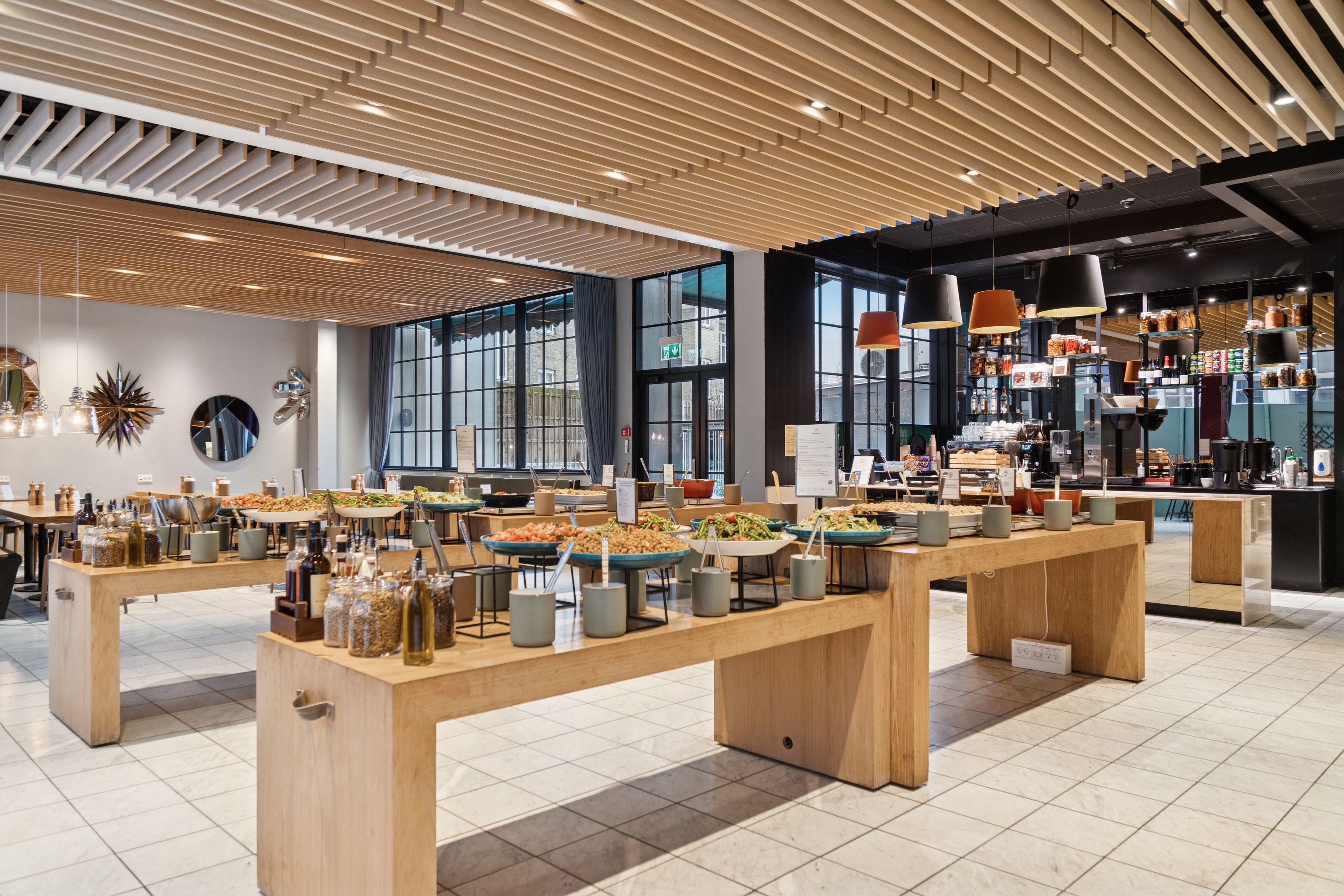 Kontorlokation med lyse lofter og moderne bord med salatbuffet og krydderier. Vinduesudsigt med store glasruder og mørke gardiner. Indkøbsmuligheder med kafe og butikker.