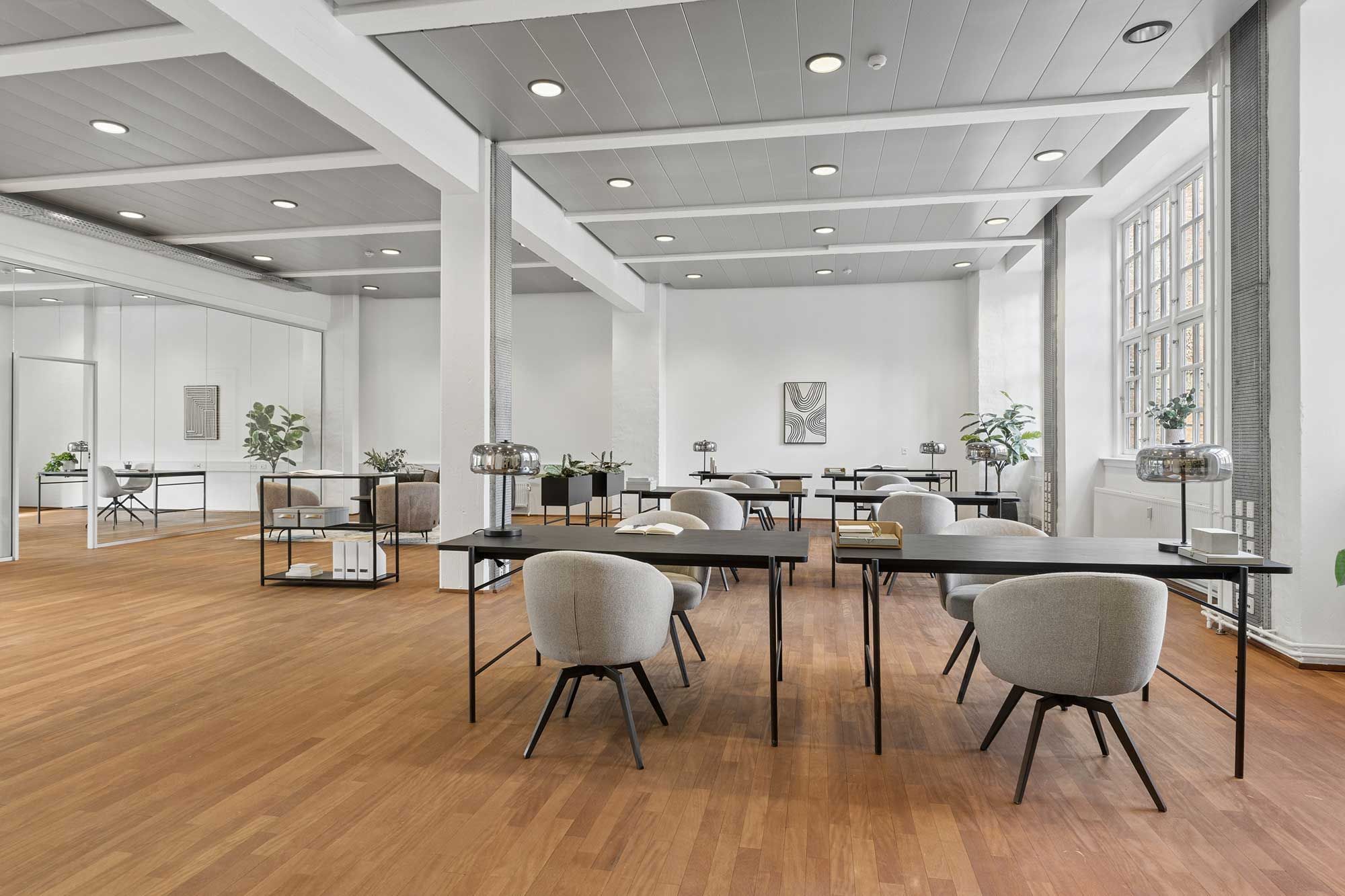 Moderne kontor med lyse trægulve og hvide vægge, smukke møbler og plante. Værelse med vinduer, hvor der er et bord med lampe og stol.