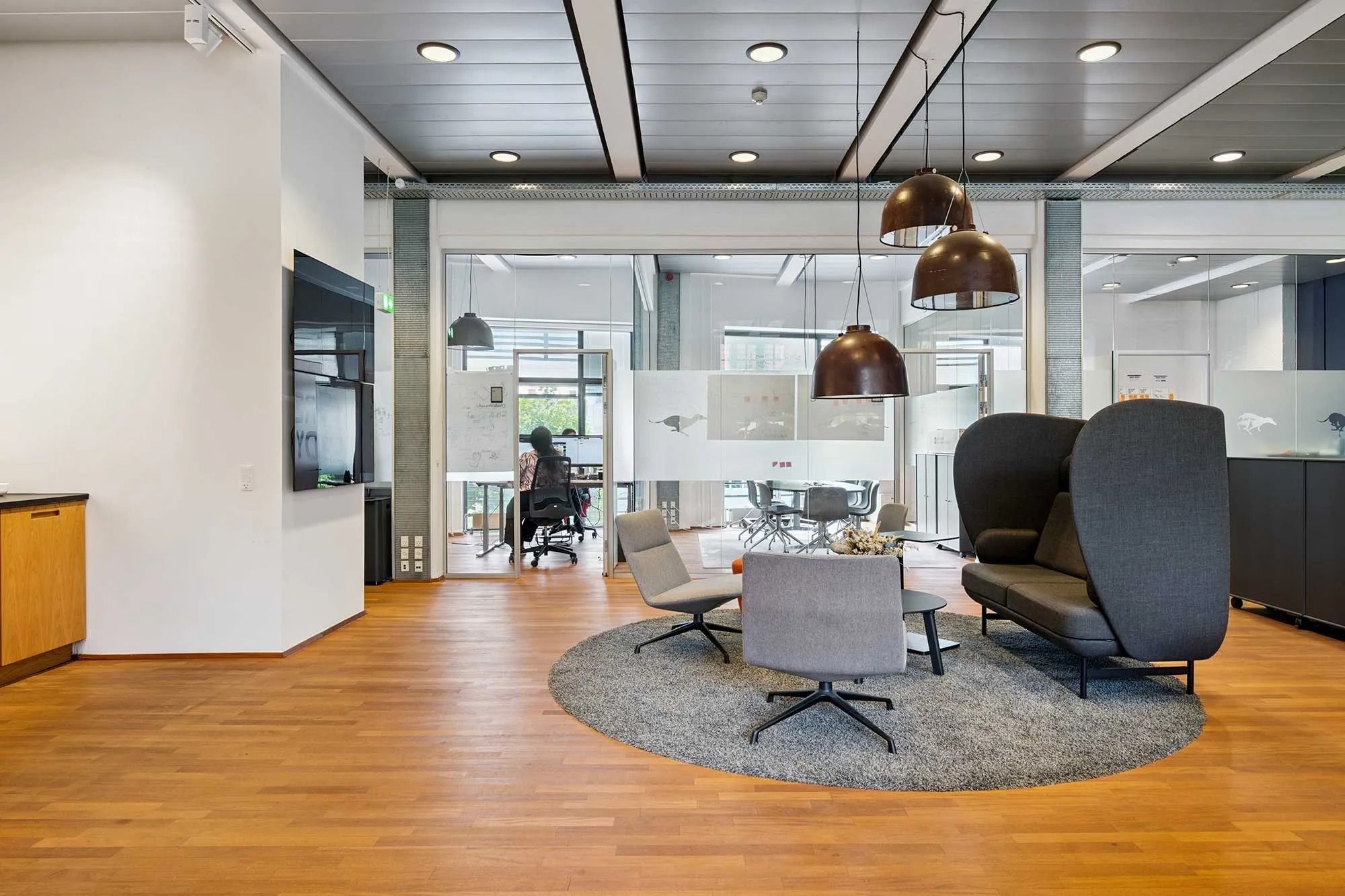 Moderne kontor med højloft, åbne områder og lyse loftslamper, samt en gruppe kontormøbler og en person i en kørestole